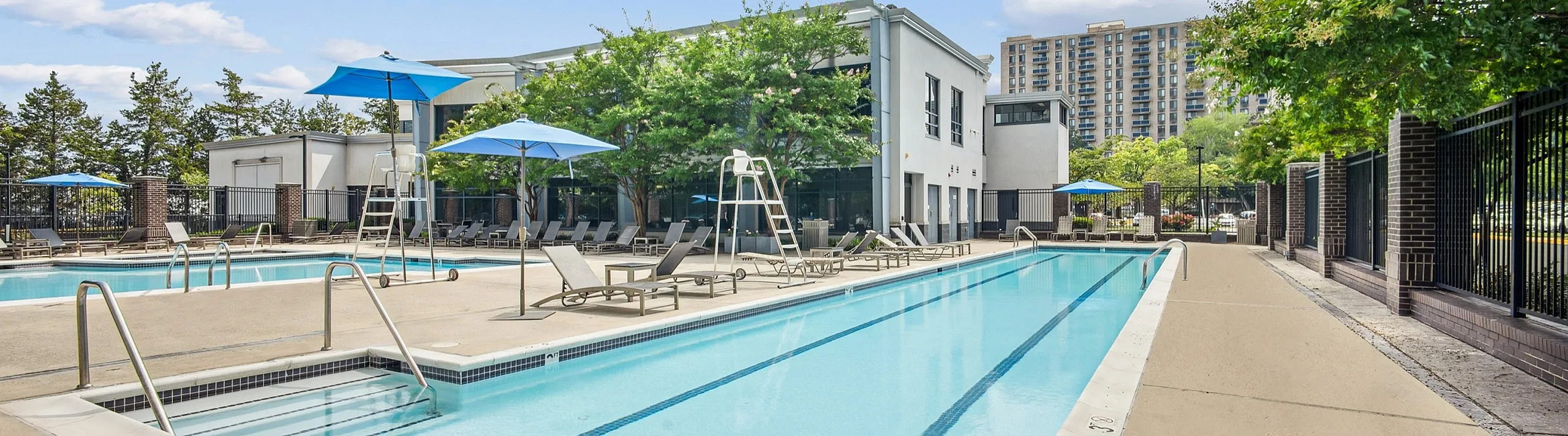 Elegant residential pool area with crystal-clear water, surrounded by stylish loungers and blue umbrellas, perfect for relaxation and leisure.