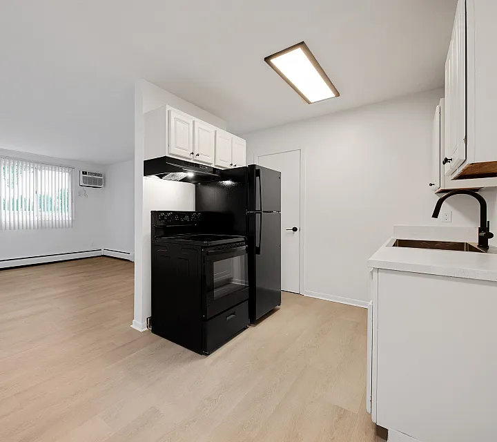 Bright and modern open-plan kitchen and living area with sleek black appliances, chic white cabinetry, and elegant natural wood flooring.