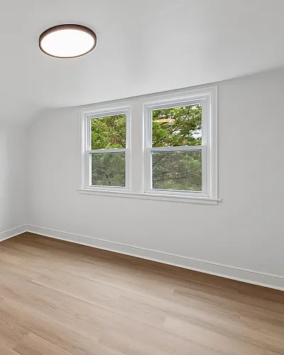 Bright and spacious minimalist room with elegant hardwood flooring, natural light from large windows, and a classic white door.
