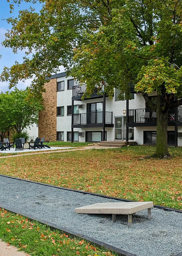 Charming apartment community with spacious outdoor lounging area, lush green lawns, and mature trees creating a serene atmosphere.