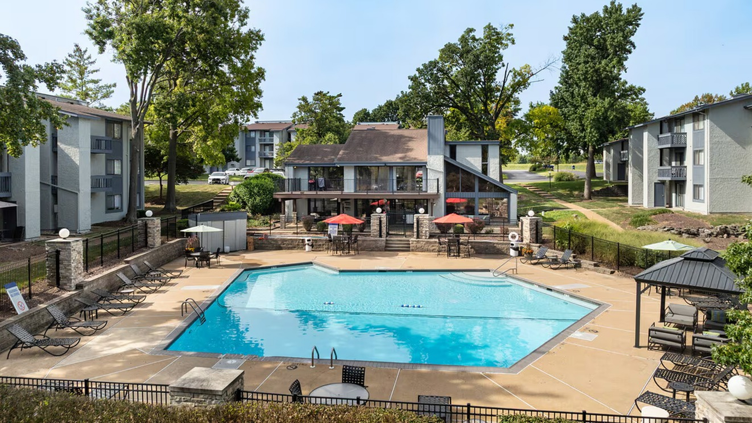 Inviting apartment complex featuring a sparkling outdoor pool surrounded by sun loungers and lush greenery.