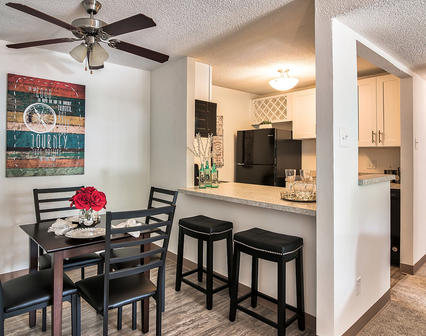 Chic apartment dining area with modern decor, featuring a stylish table set with red roses, adjacent to an inviting open-plan kitchen and breakfast bar with sleek barstools.