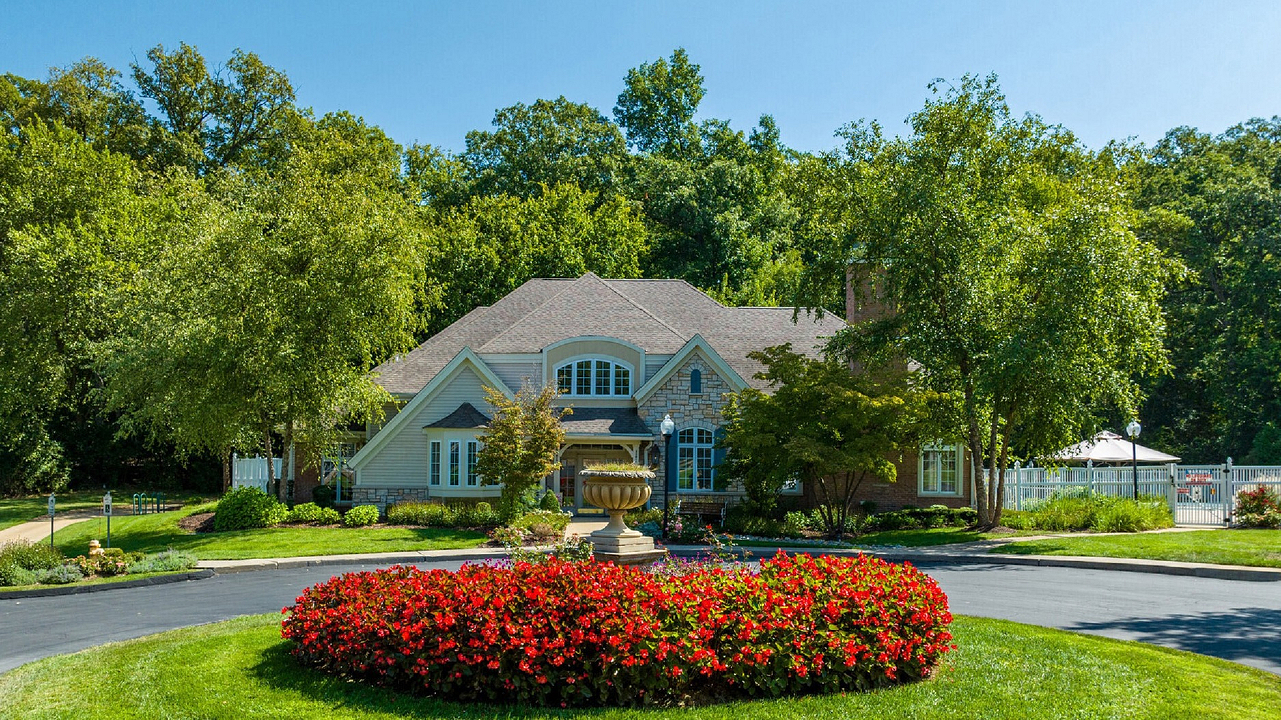 Charming house with a beautifully landscaped front yard featuring vibrant red flowers and lush greenery surrounded by mature trees.