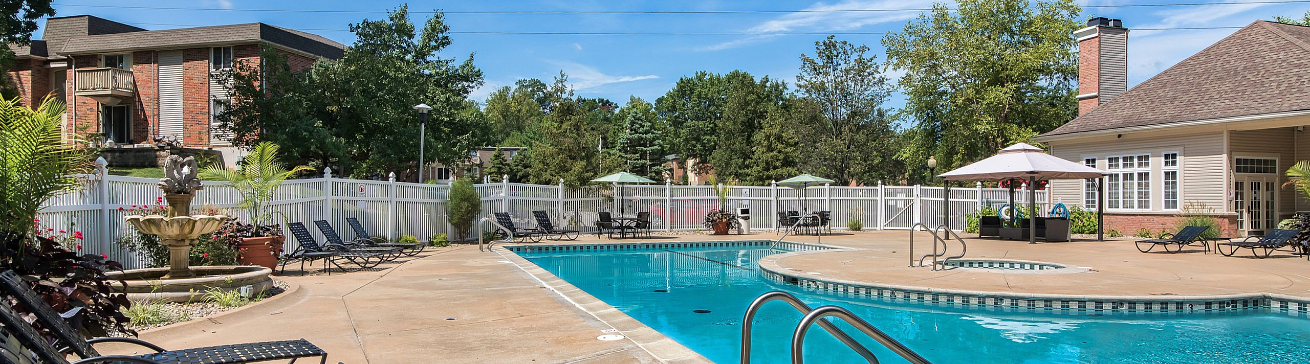 Inviting outdoor pool area with lounge chairs, vibrant landscaping, and a charming fountain under a clear blue sky.