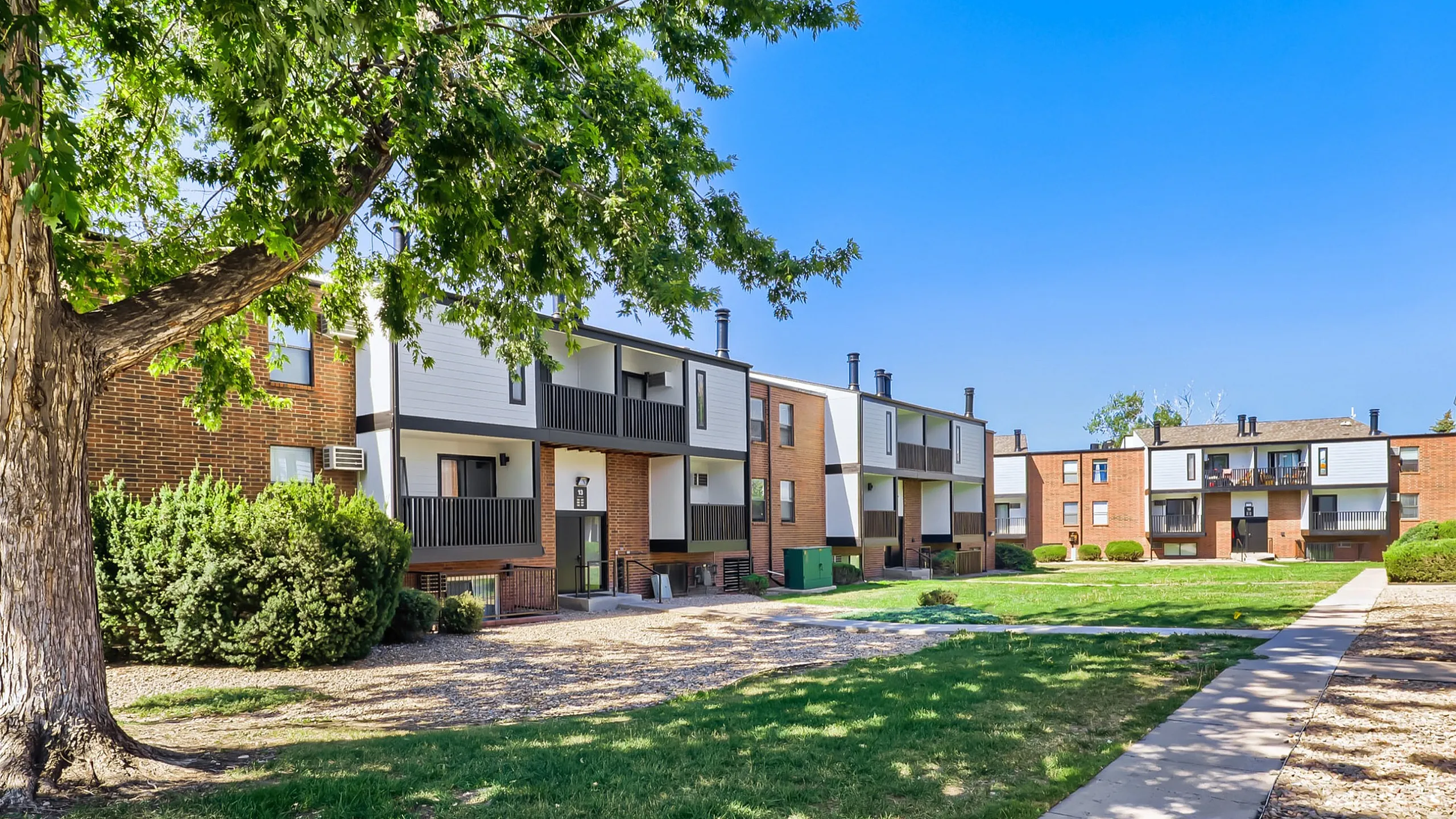 Charming apartment complex with modern brick facade, lush green spaces, and abundant natural light for a tranquil living experience.