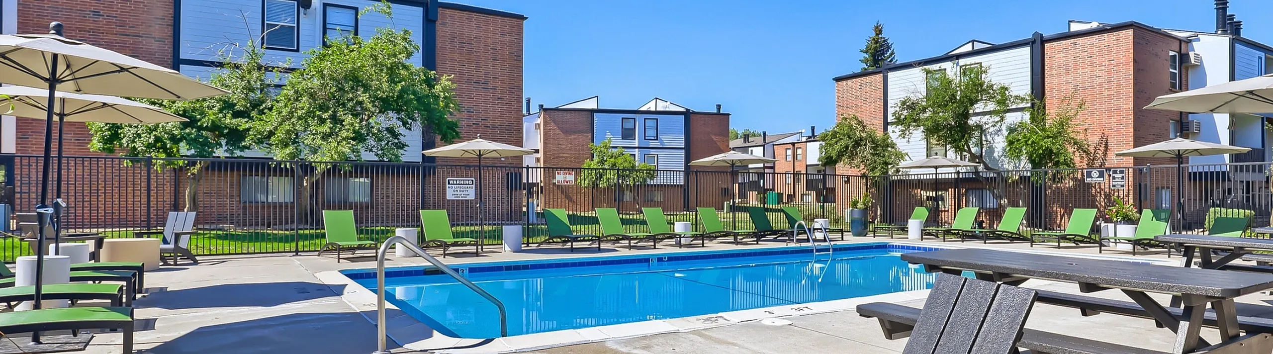 Inviting apartment complex pool area with sun loungers, umbrellas, and modern brick buildings, perfect for relaxation and leisure.