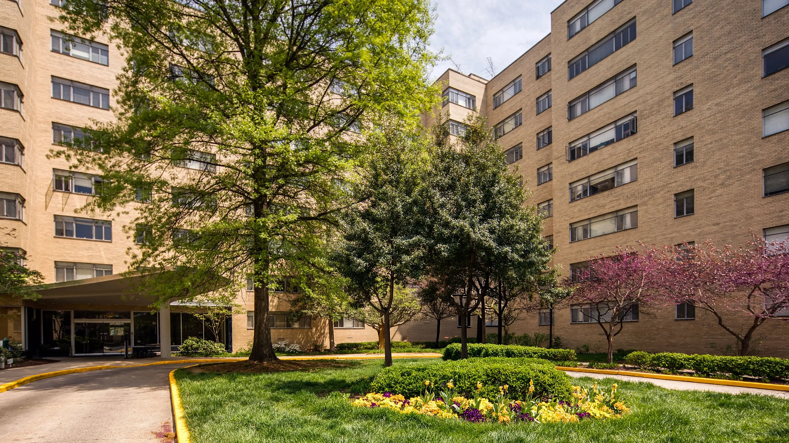 Inviting apartment complex exterior with lush landscaped gardens, vibrant trees, and a welcoming entrance.