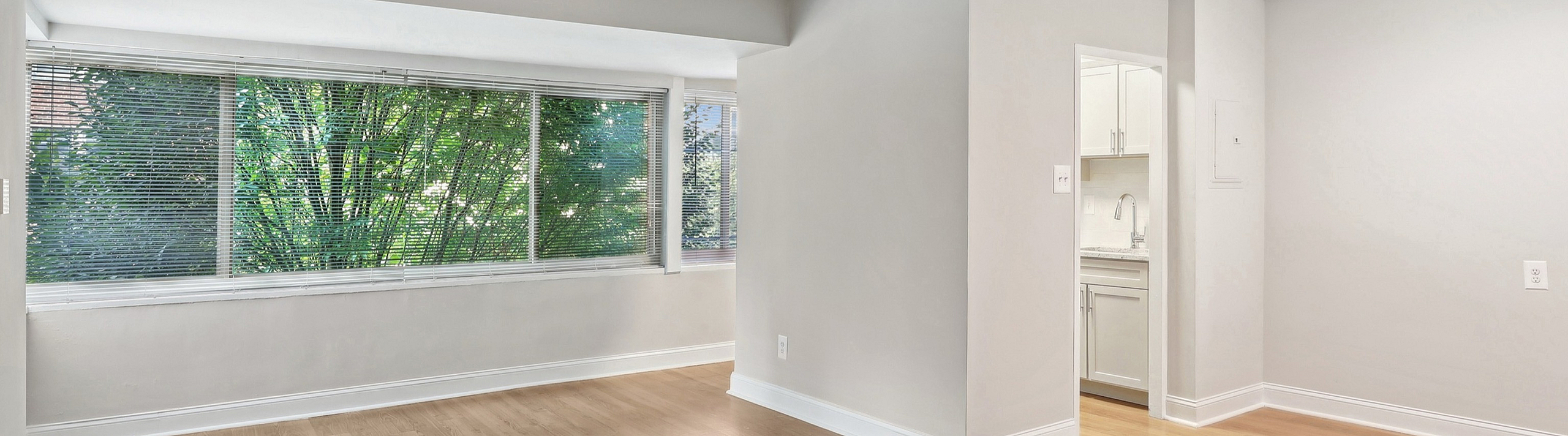 Bright, open-concept living area with large windows and modern kitchen entry, featuring elegant hardwood flooring.