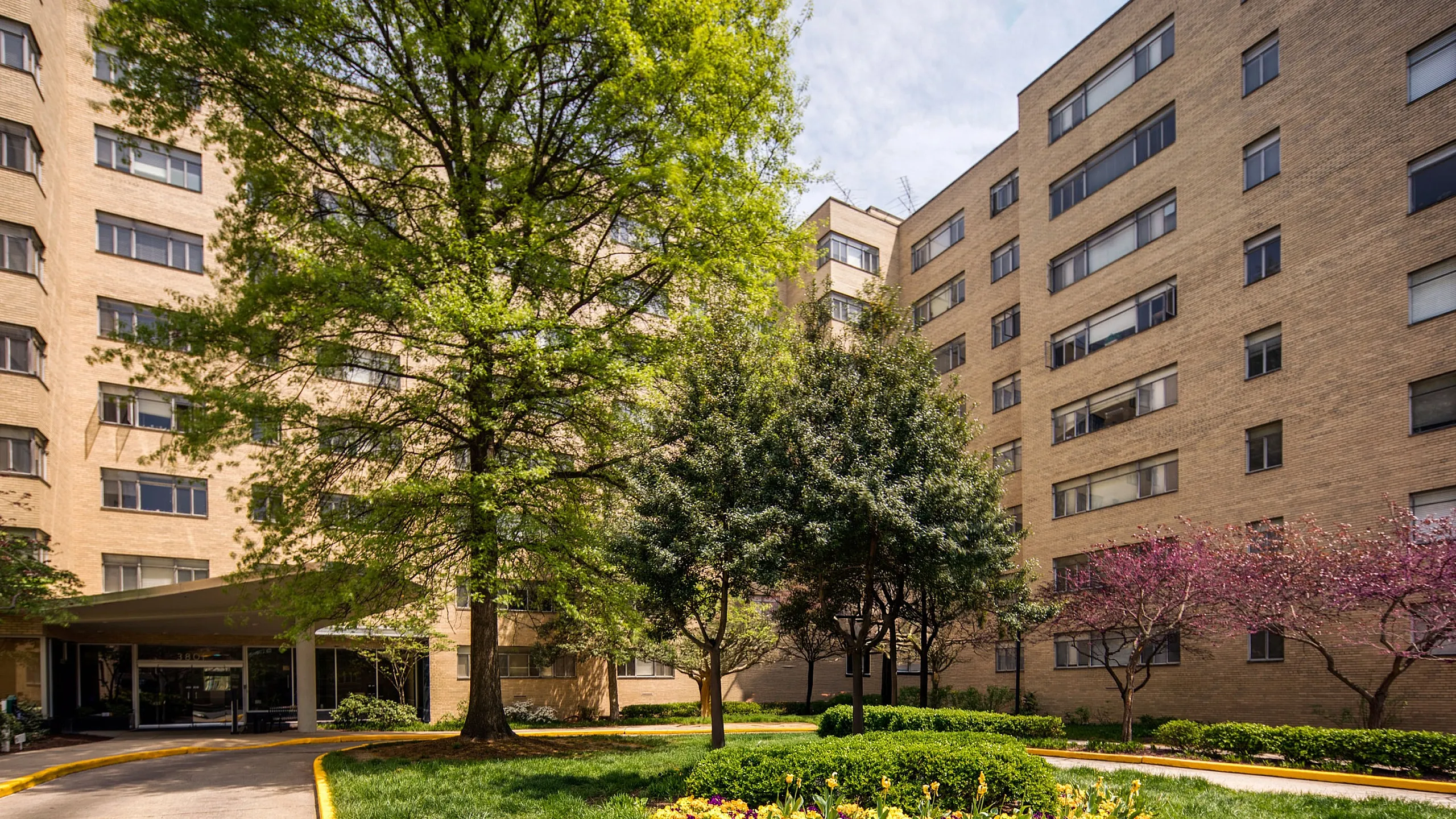 Inviting apartment complex with lush green landscaping, vibrant flowerbeds, and mature trees enhancing the serene atmosphere.