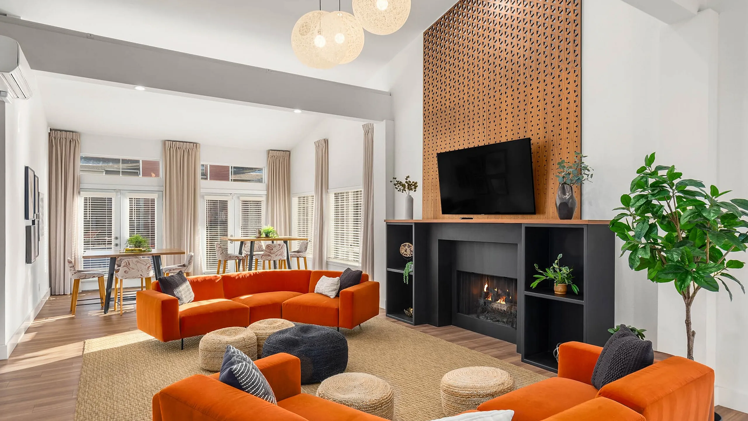 Inviting modern living room with vibrant orange sofas, elegant fireplace, and abundant natural light from large windows.