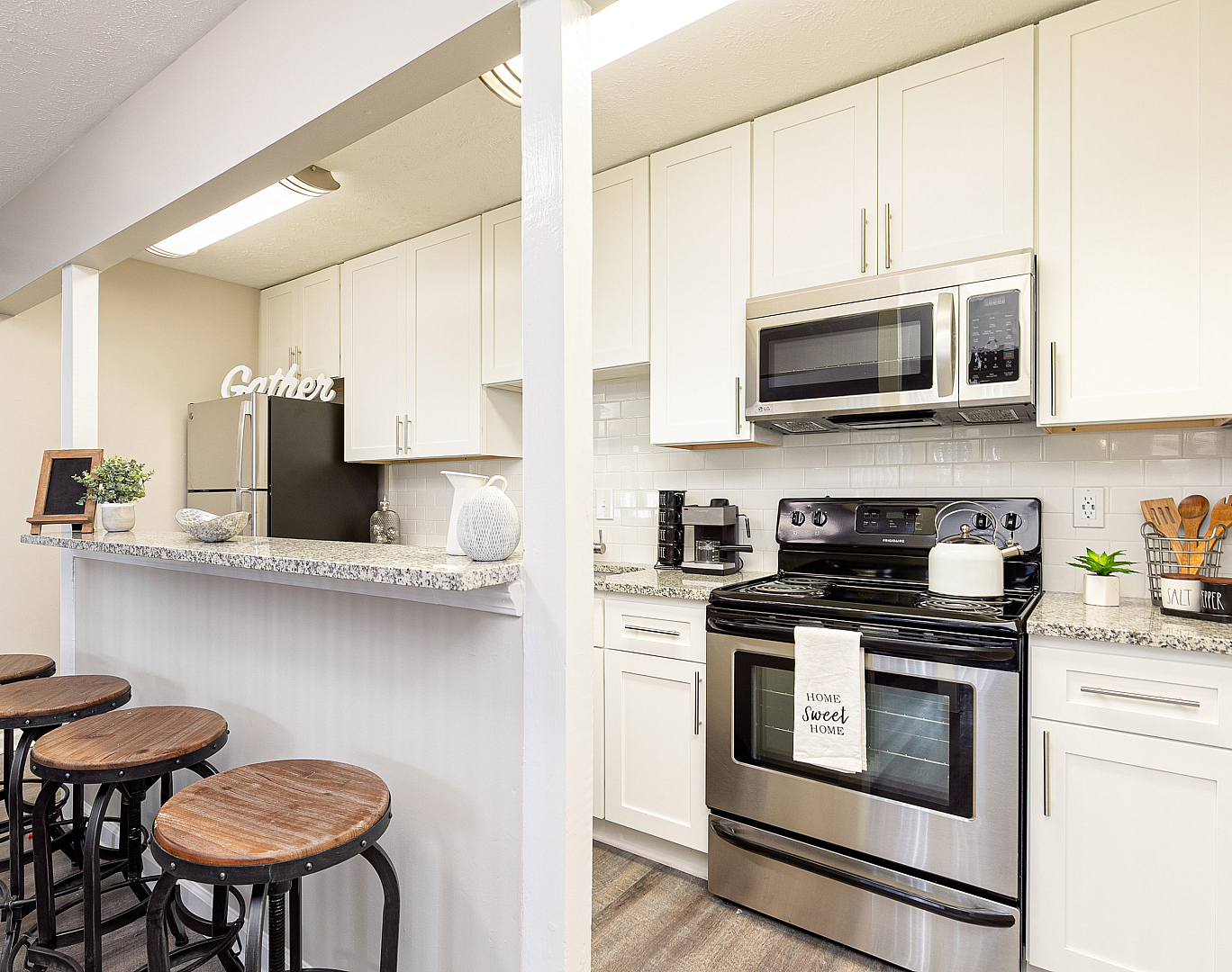 Modern kitchen with sleek stainless steel appliances, elegant white cabinetry, and a chic granite countertop bar with stylish wooden stools.