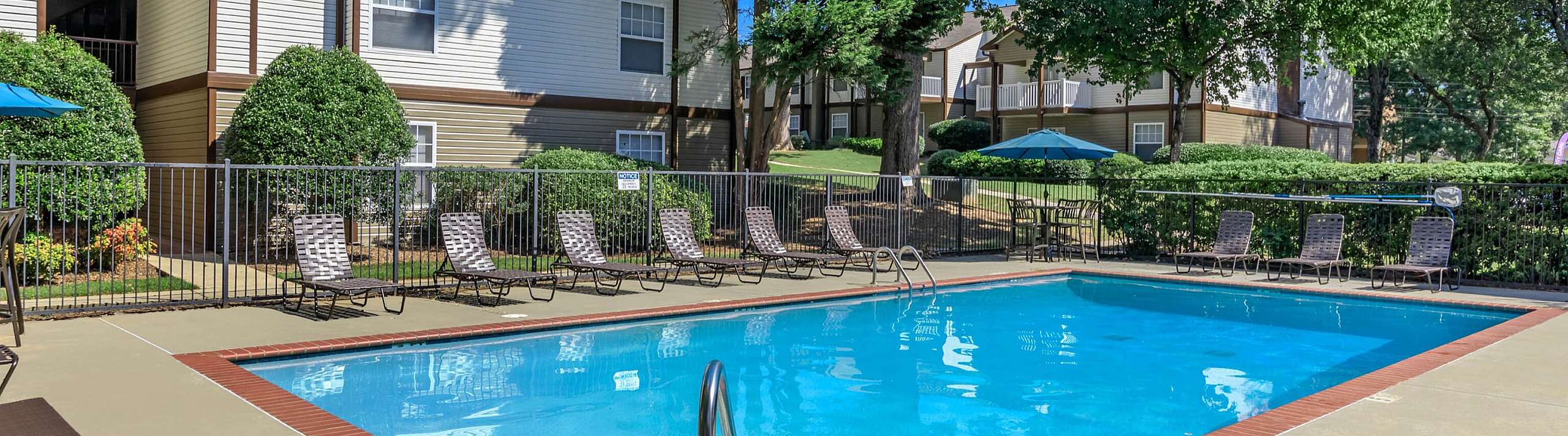 Inviting apartment complex with a sparkling swimming pool and lush greenery, perfect for relaxation.
