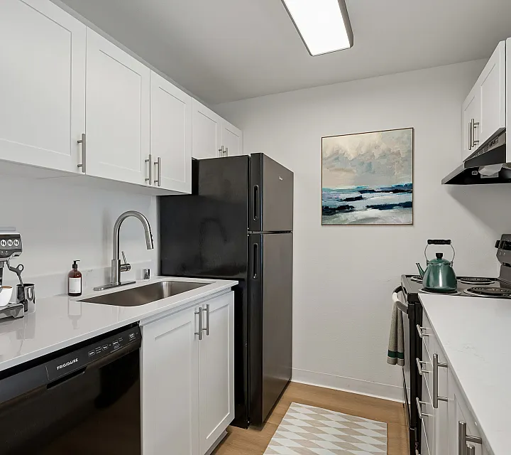 Modern kitchen with sleek black appliances, elegant white cabinets, and stylish artwork.
