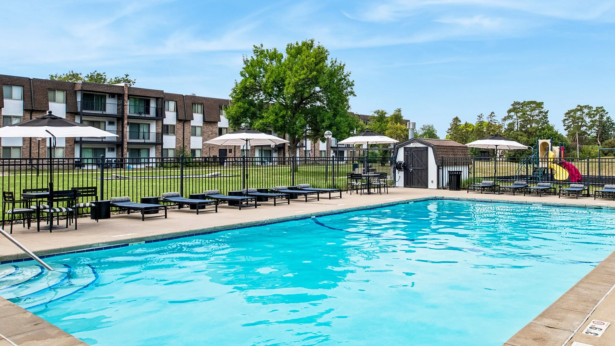 Inviting community pool area with sun loungers, umbrellas, and a nearby playground, perfect for family relaxation.