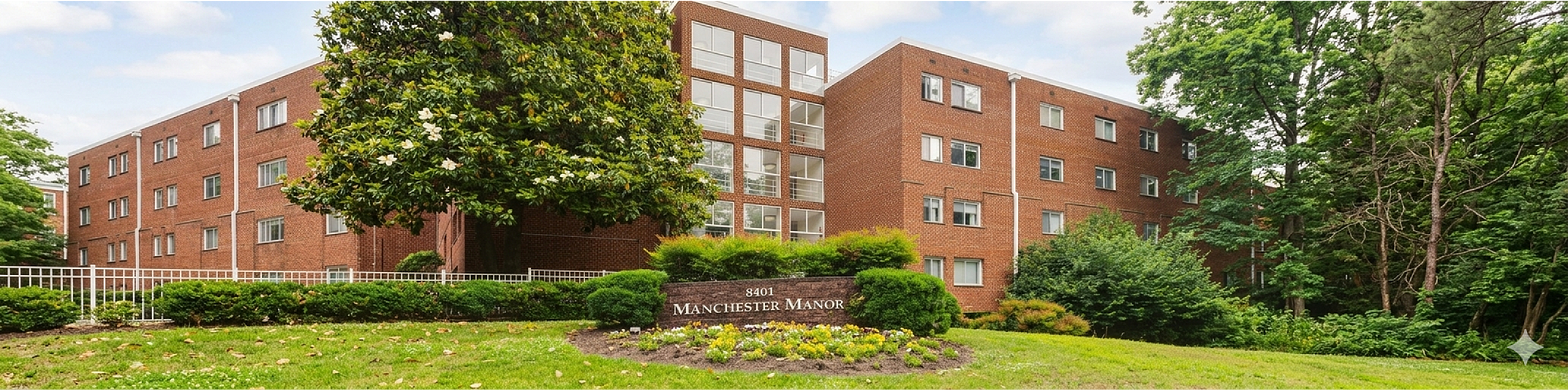 Charming brick apartment building surrounded by lush greenery, featuring serene outdoor spaces and a welcoming atmosphere at Manchester Manor.