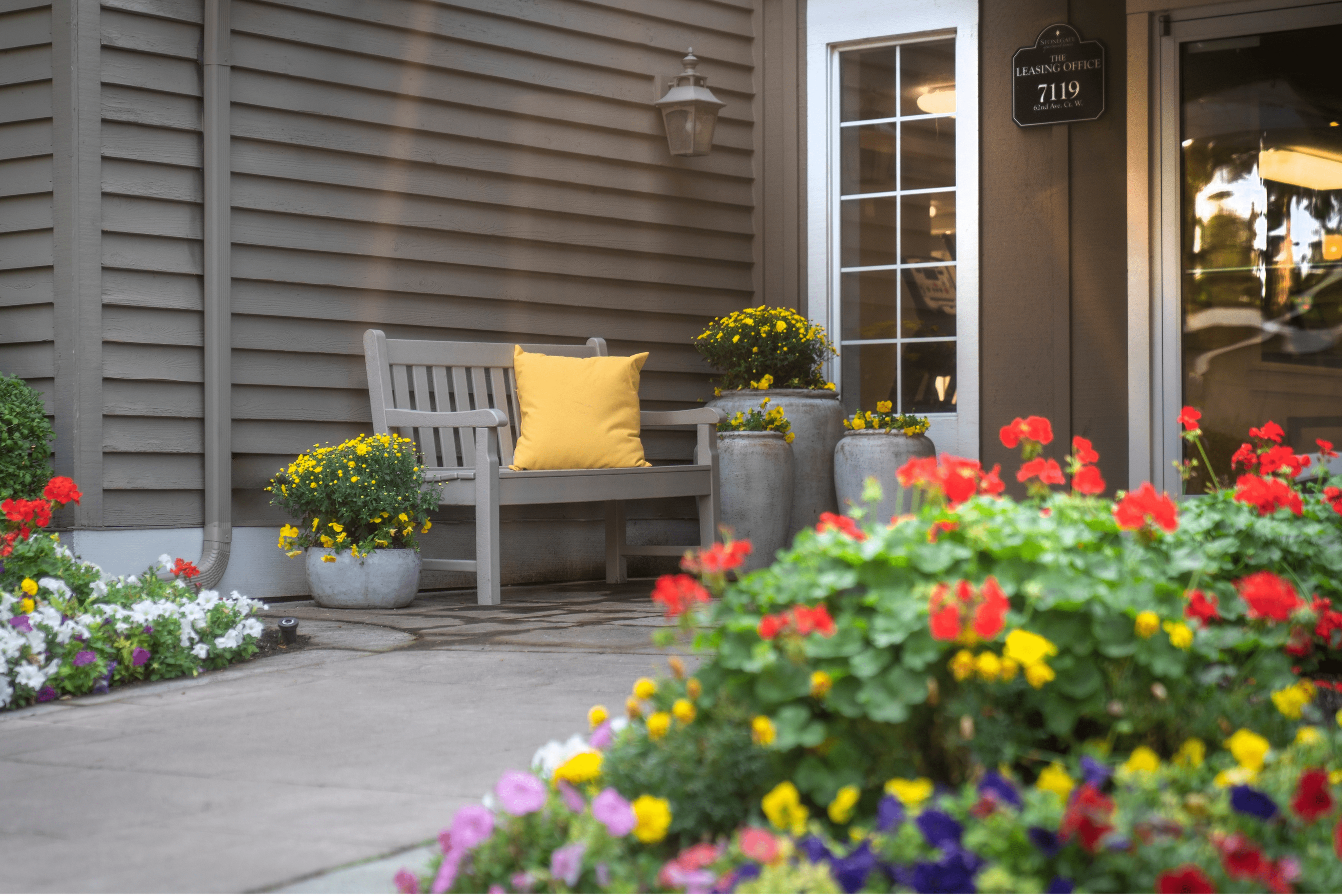 Inviting apartment entrance with vibrant flowers, a wooden bench, and a cheerful yellow pillow.