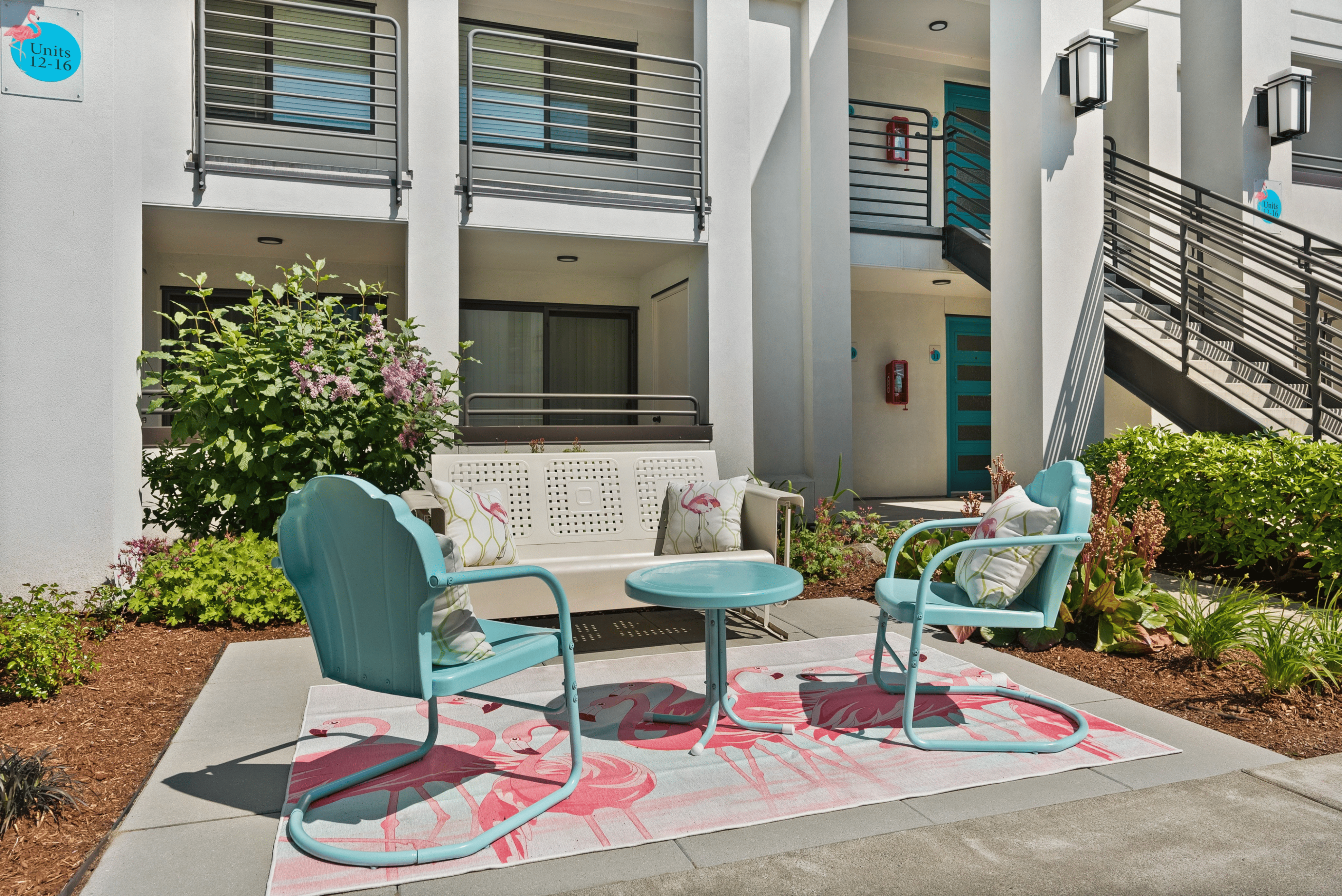 Charming outdoor seating area with turquoise chairs and a flamingo-themed rug, set against a modern apartment backdrop.
