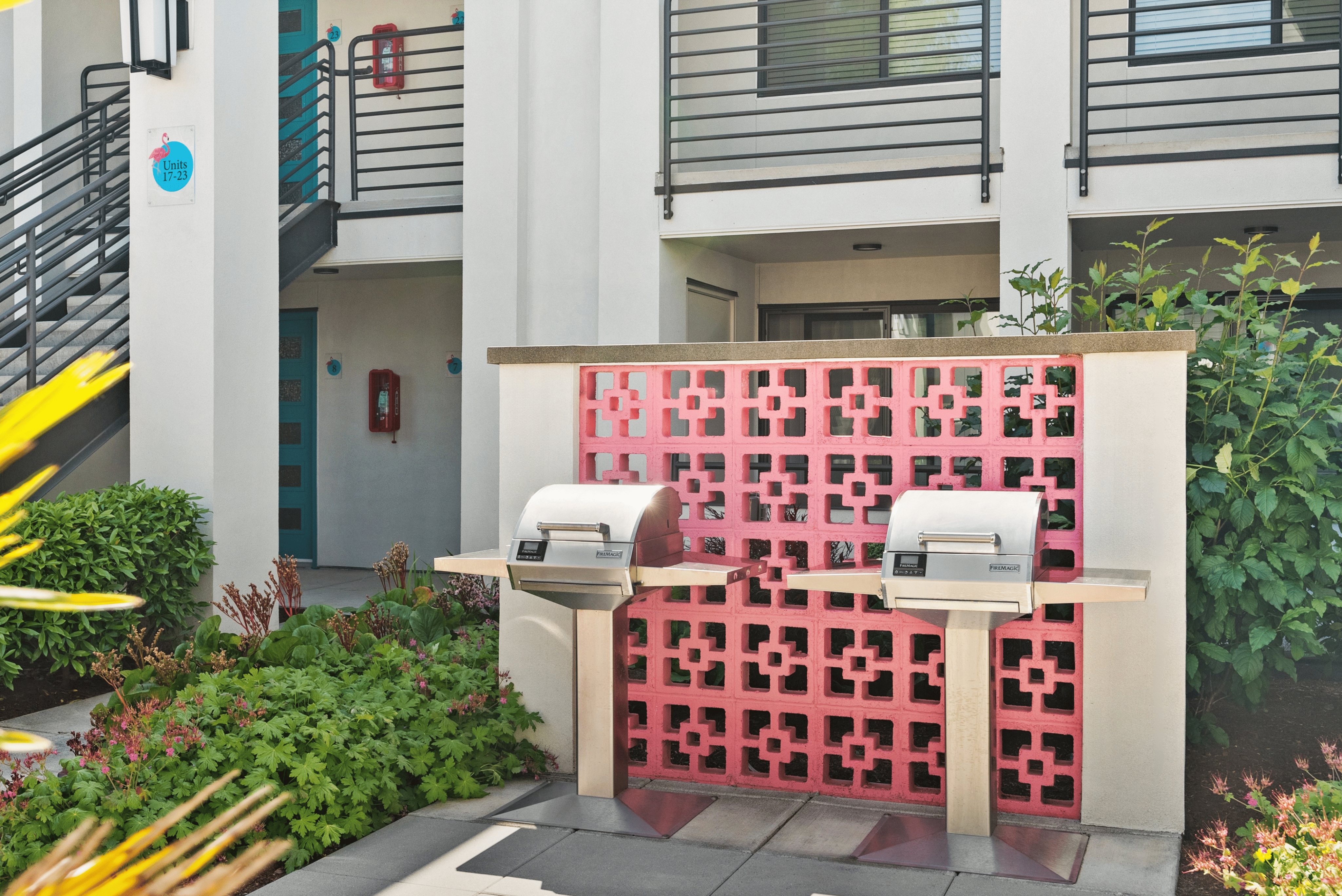 Charming apartment complex with stylish outdoor BBQ area, accented by a vibrant pink decorative wall and lush greenery.