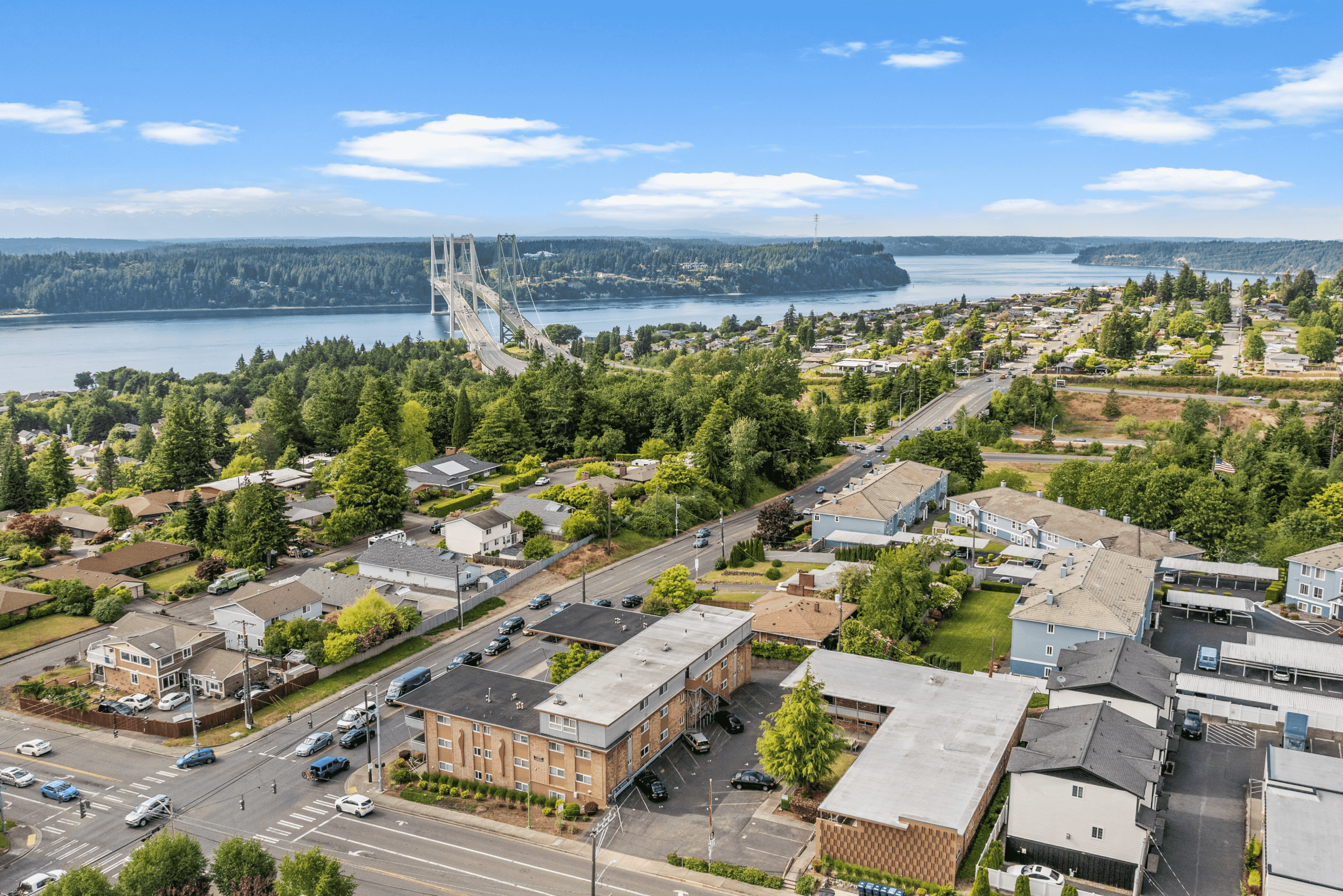 Breathtaking aerial view of a scenic neighborhood featuring lush greenery, a vibrant community, and stunning water views with an impressive bridge in the background.