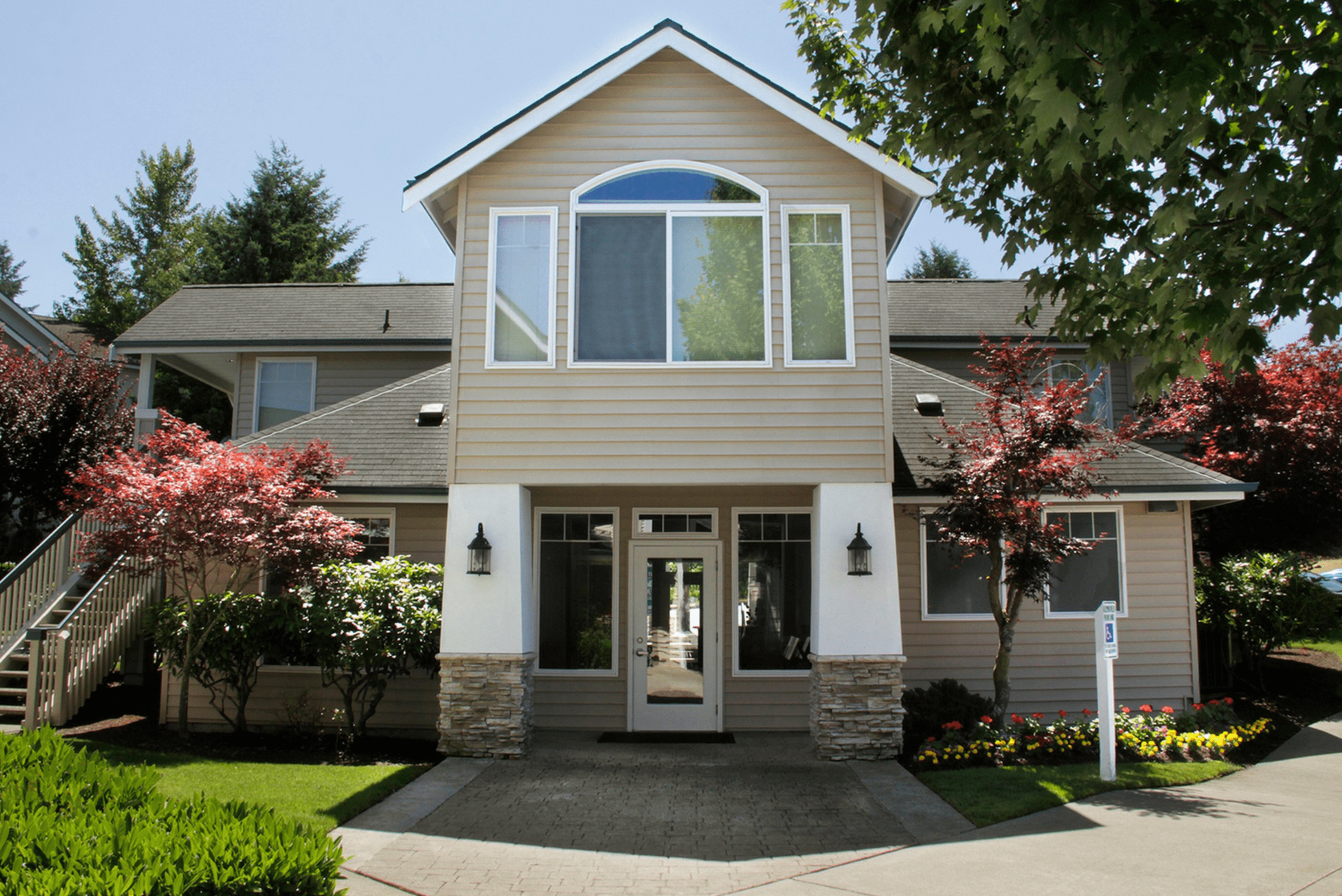 Charming two-story home with elegant stone accents, surrounded by vibrant landscaping and mature trees.