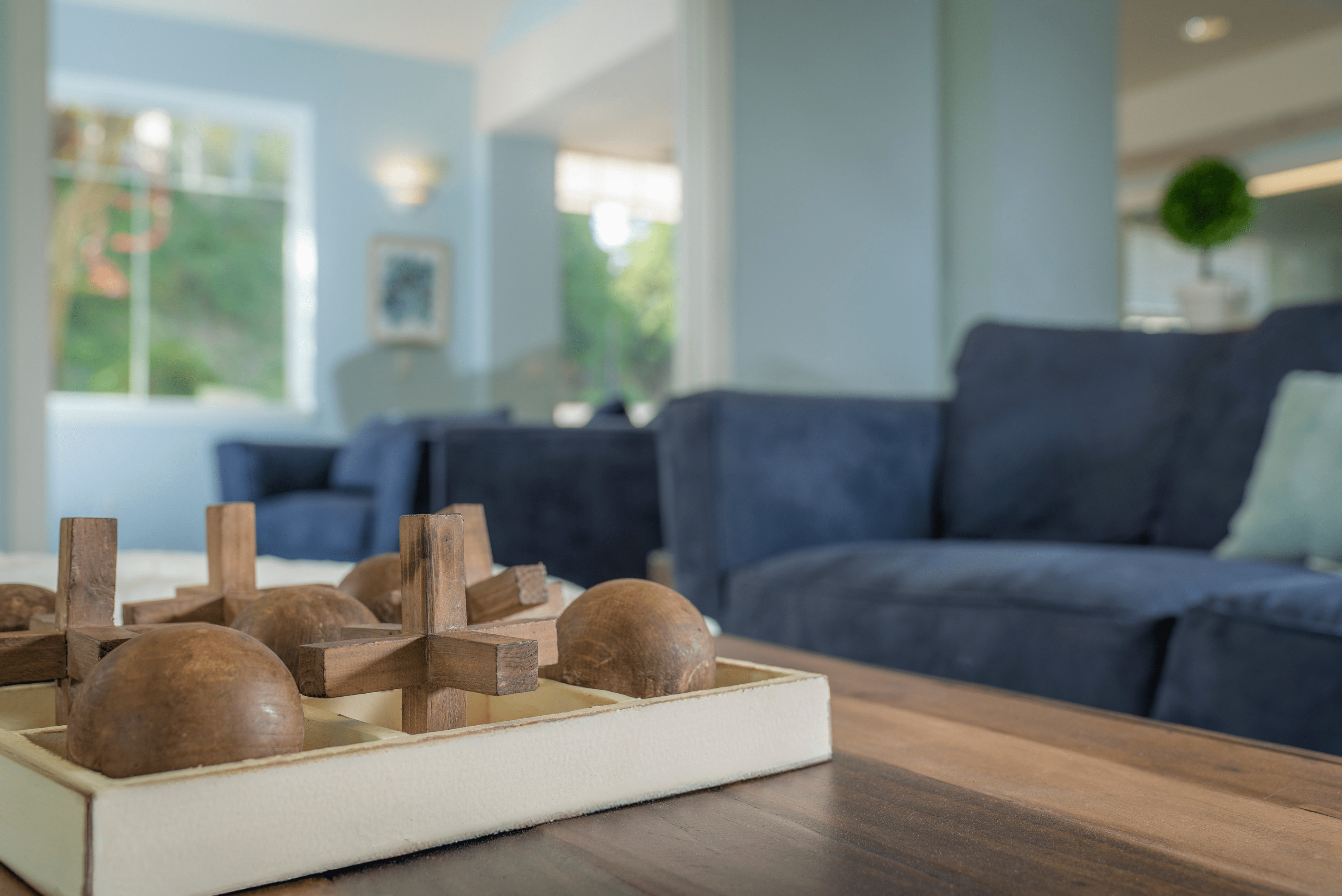 Inviting living room with plush blue sofas and a modern wooden centerpiece, filled with natural light from large windows and elegant decor.