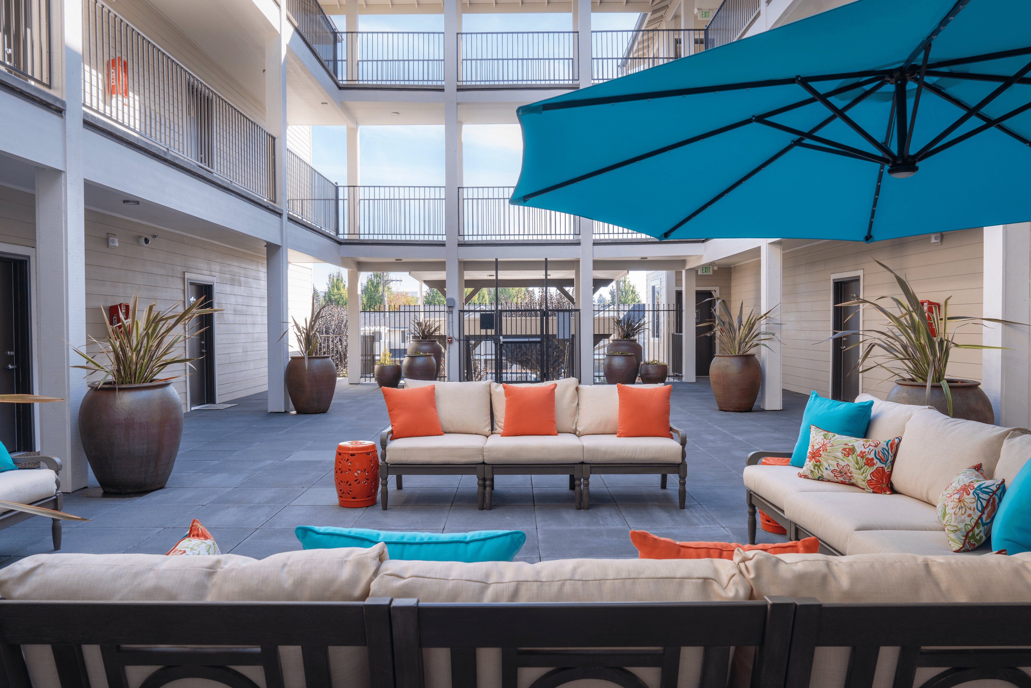 Inviting outdoor lounge space with stylish seating, vibrant cushions, large planters, and expansive blue umbrella for shaded relaxation.
