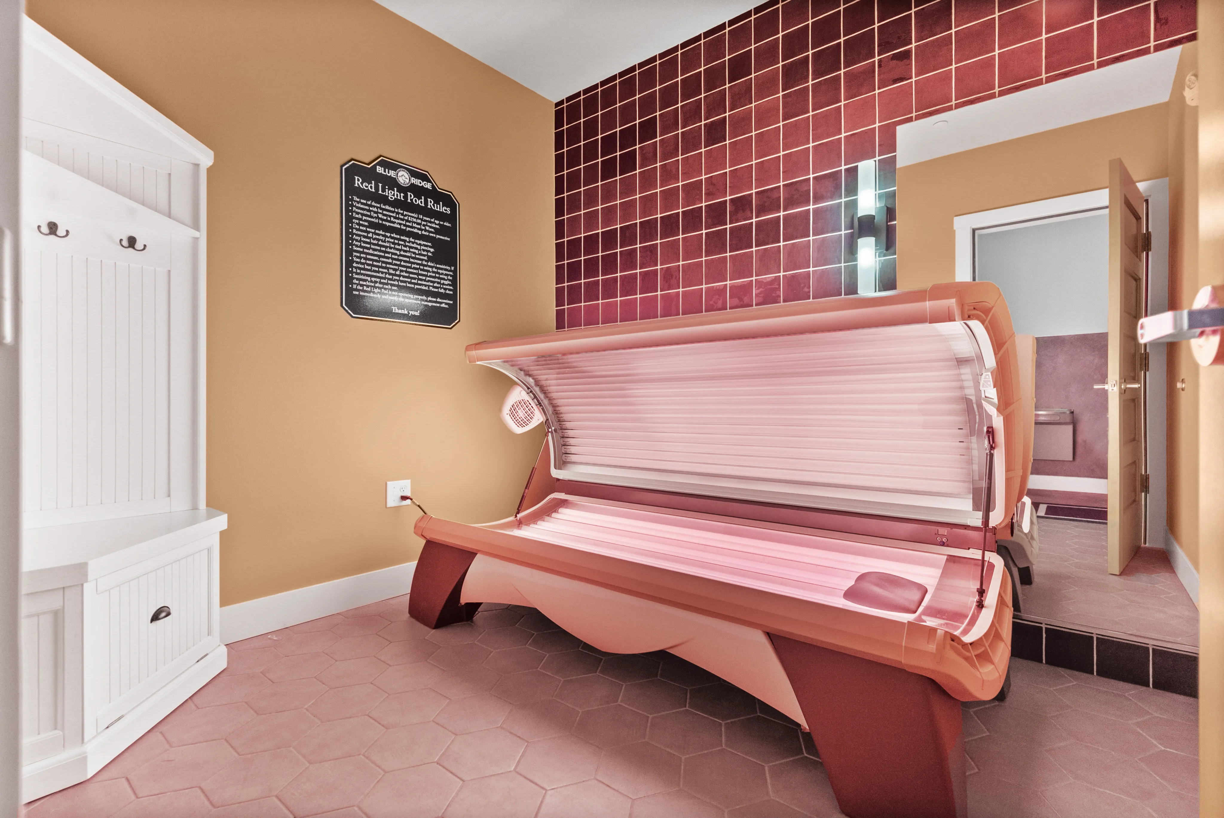 Modern wellness room featuring a sleek red light therapy bed, warm tile accents, and chic wooden cabinetry.