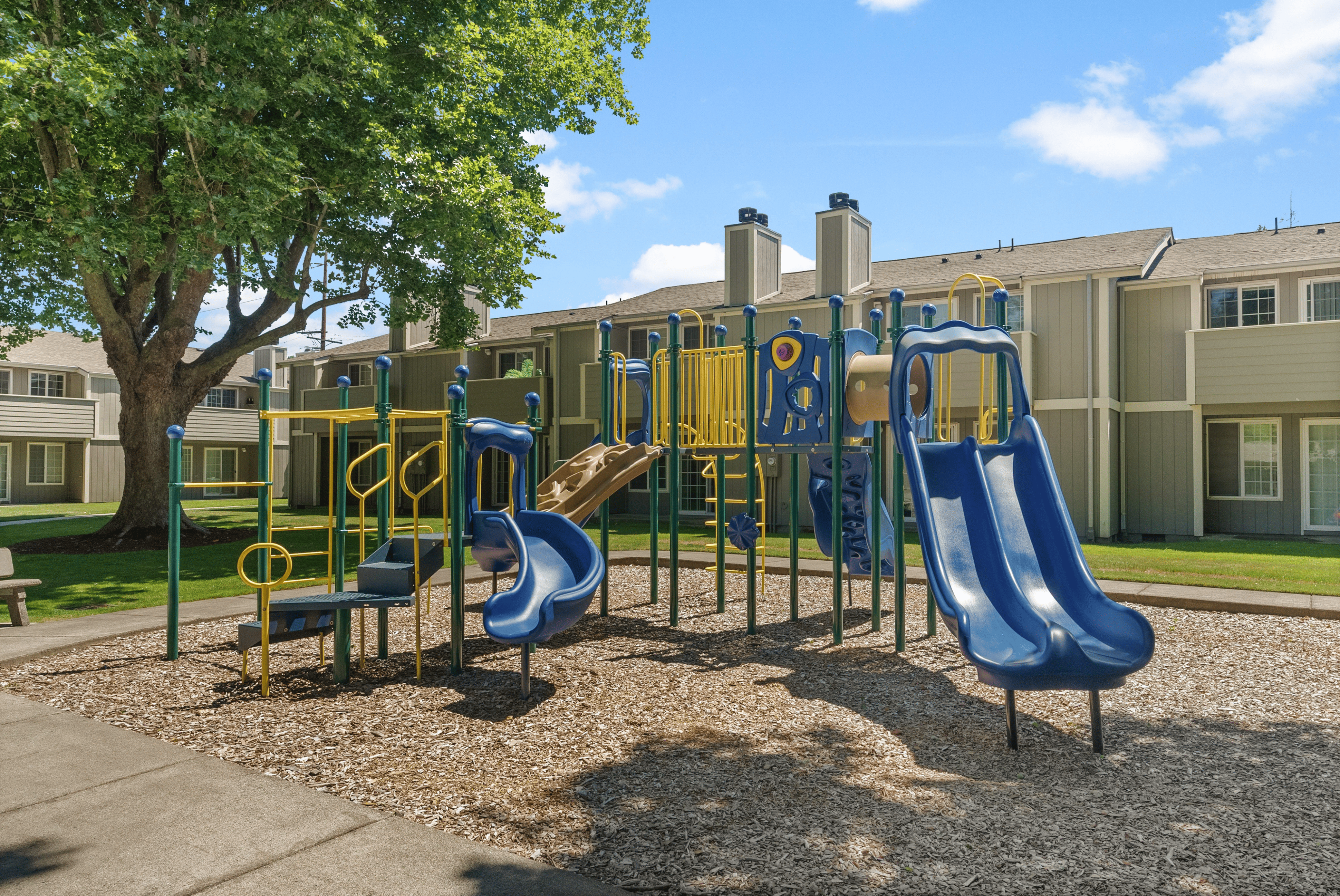 Charming apartment community featuring a vibrant playground surrounded by lush greenery and modern townhomes.