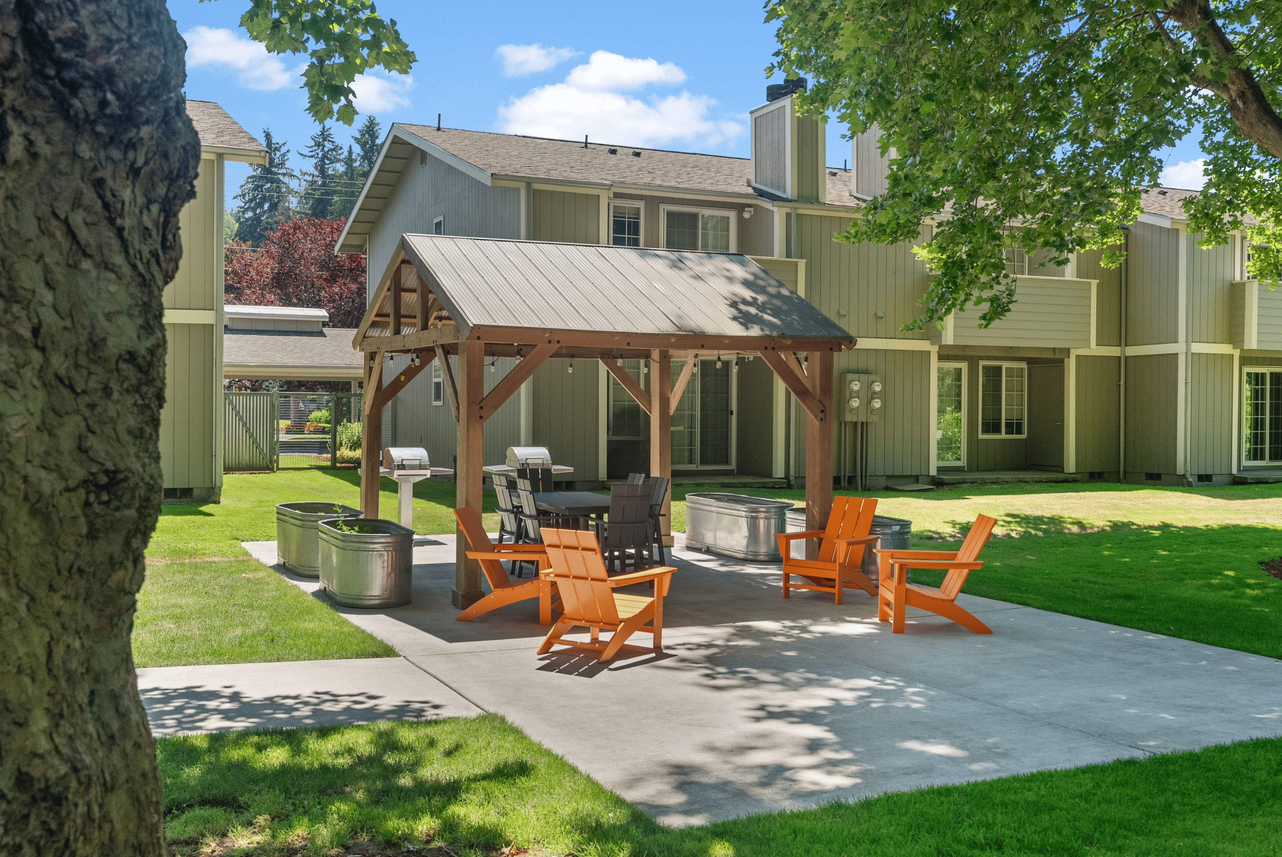 Charming outdoor communal space with cozy wooden seating, a modern pergola, and lush green surroundings, perfect for social gatherings.
