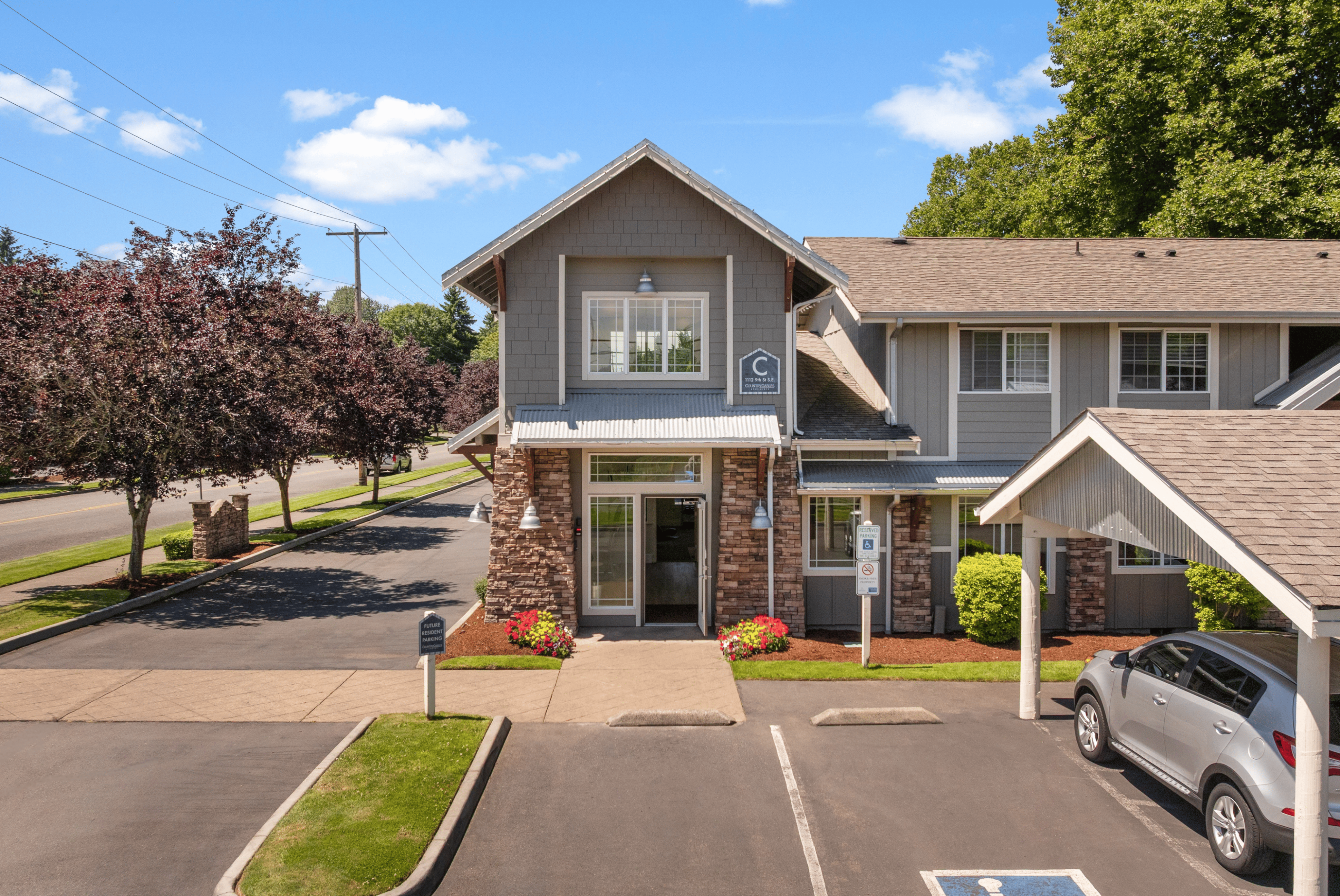 Charming suburban apartment complex with modern architecture, ample parking, and lush greenery on a sunny day.
