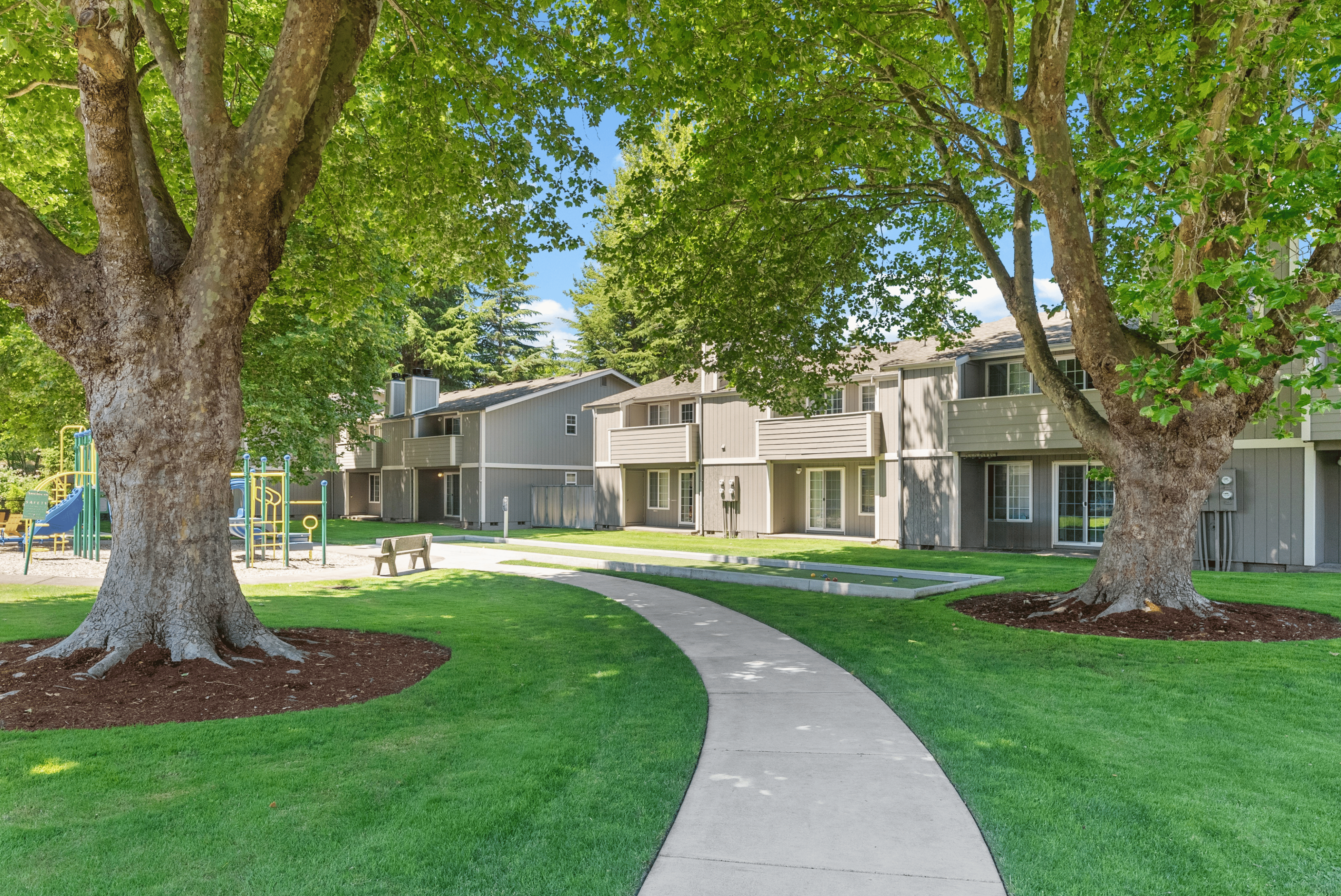 Tranquil apartment complex with lush green landscaping and charming pathways, perfect for relaxation and family-friendly community living.