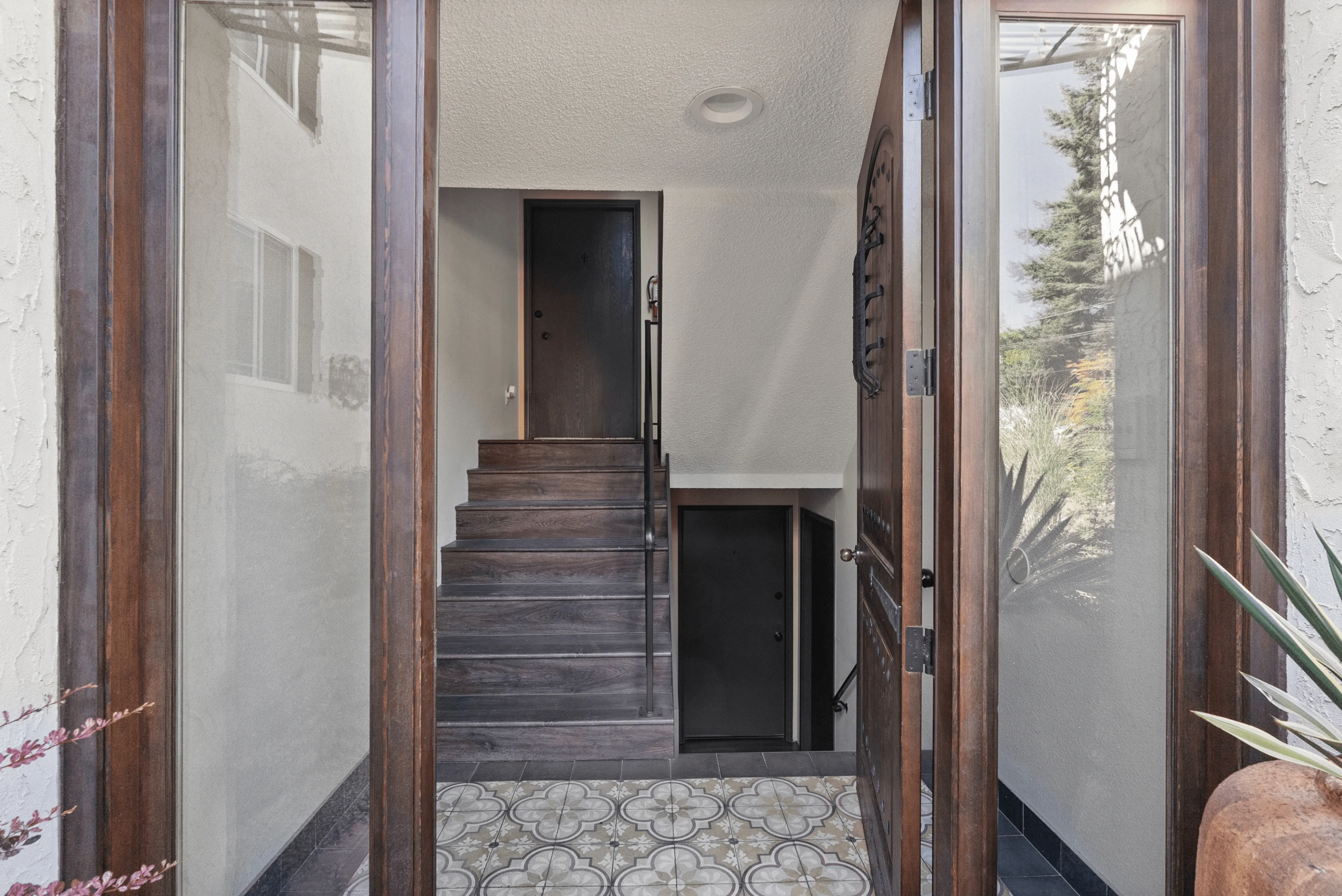 Inviting entrance with elegant wooden door and stylish tiled flooring leads into a charming interior staircase.