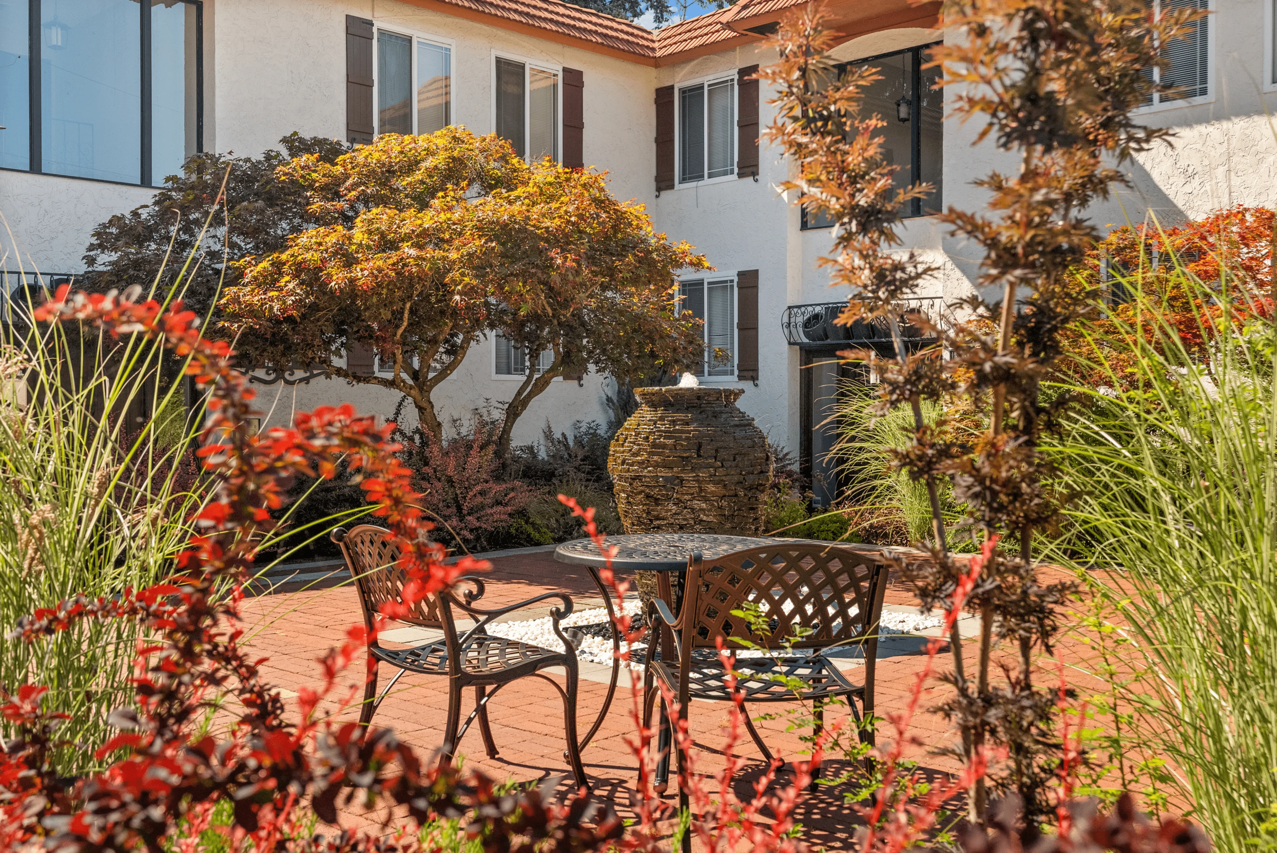 Charming apartment courtyard with elegant wrought iron furniture surrounded by lush greenery and a rustic stone fountain.