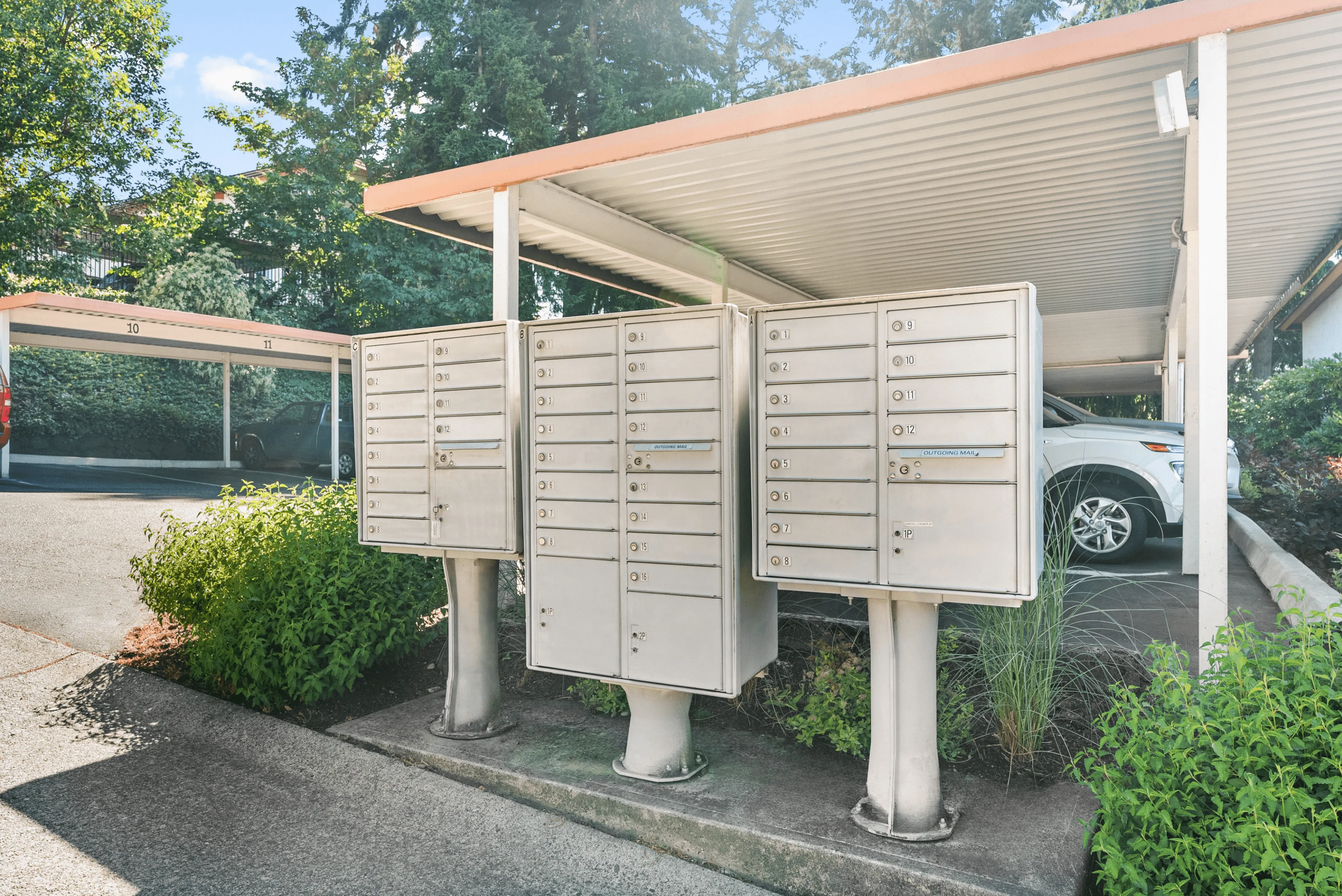 Charming outdoor mailboxes set under a covered parking area surrounded by lush greenery.