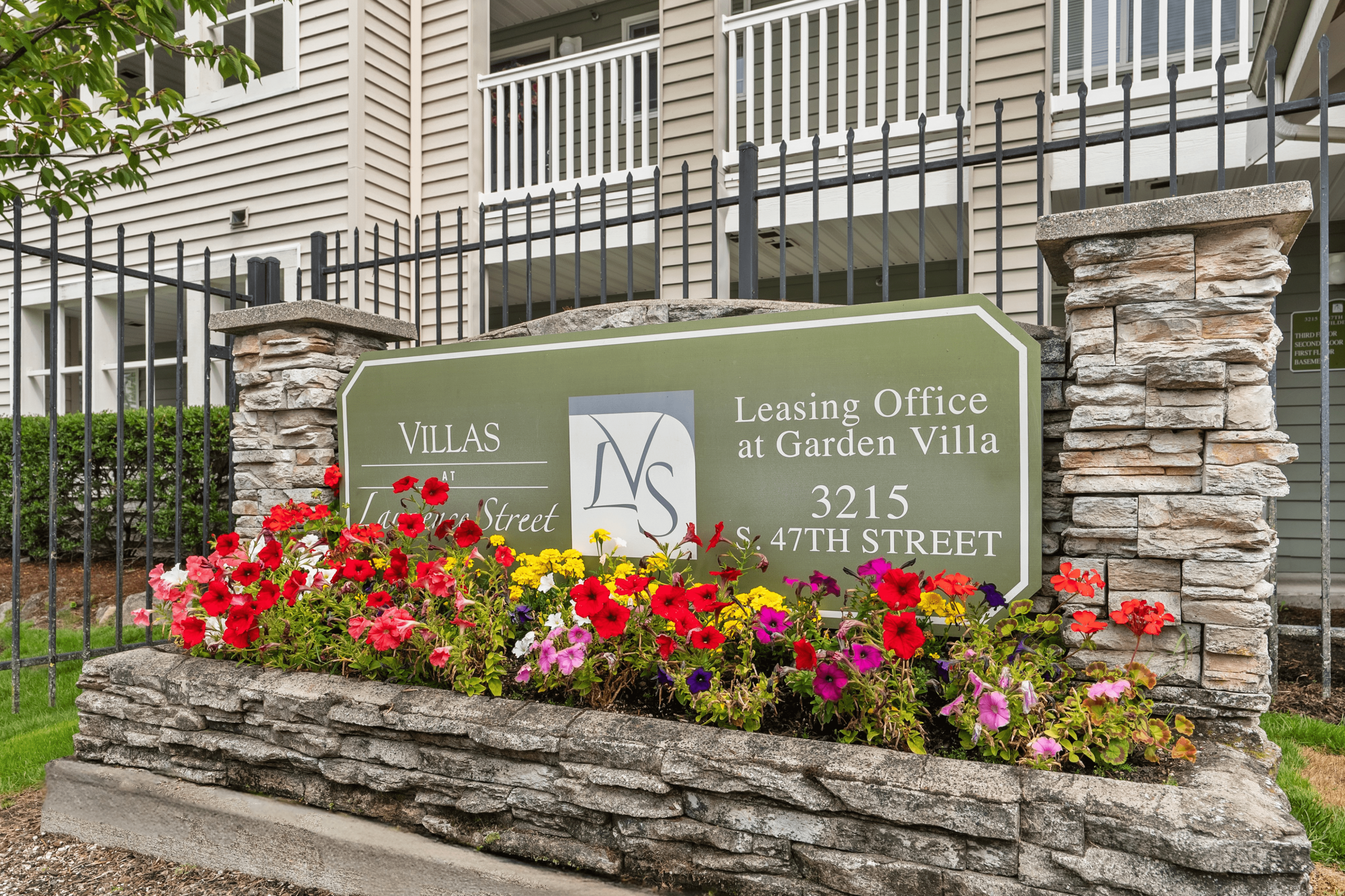 Inviting entrance to Villas at Garden Street with vibrant flower beds and elegant stonework at the leasing office.