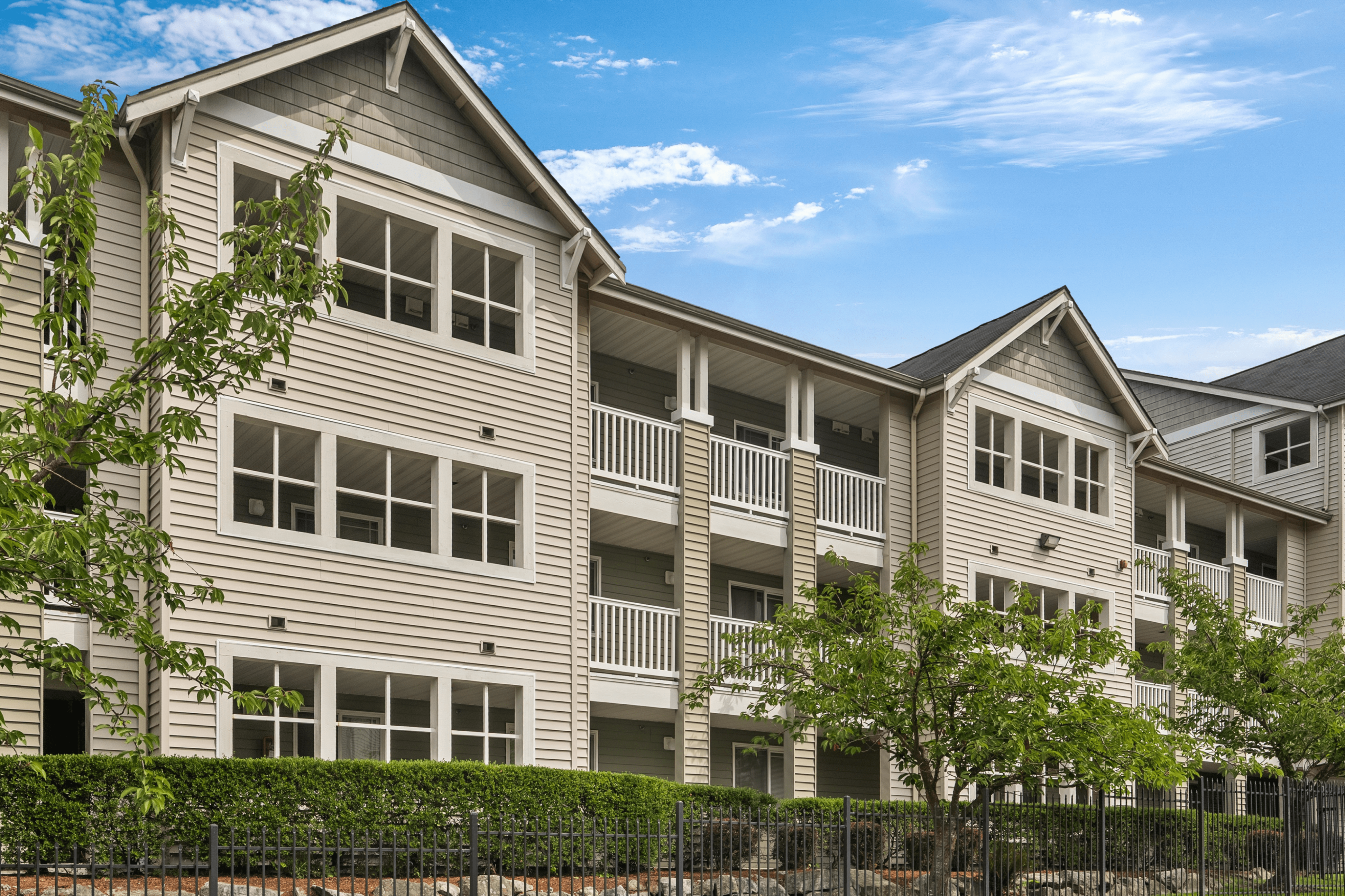 Charming three-story apartment building with inviting balconies and lush greenery under a bright blue sky.