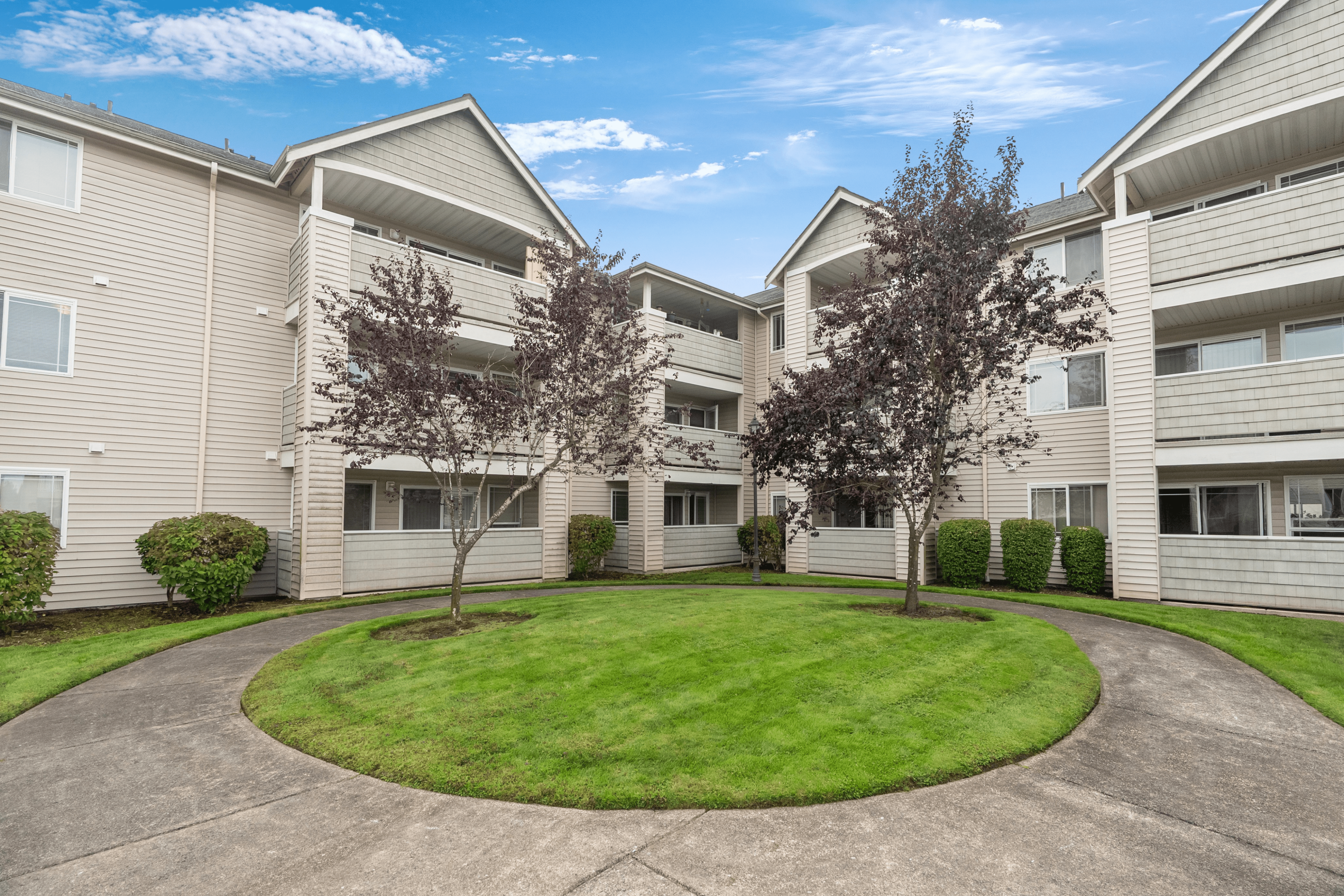 Charming apartment complex with well-maintained landscaping and inviting balconies under a bright blue sky.