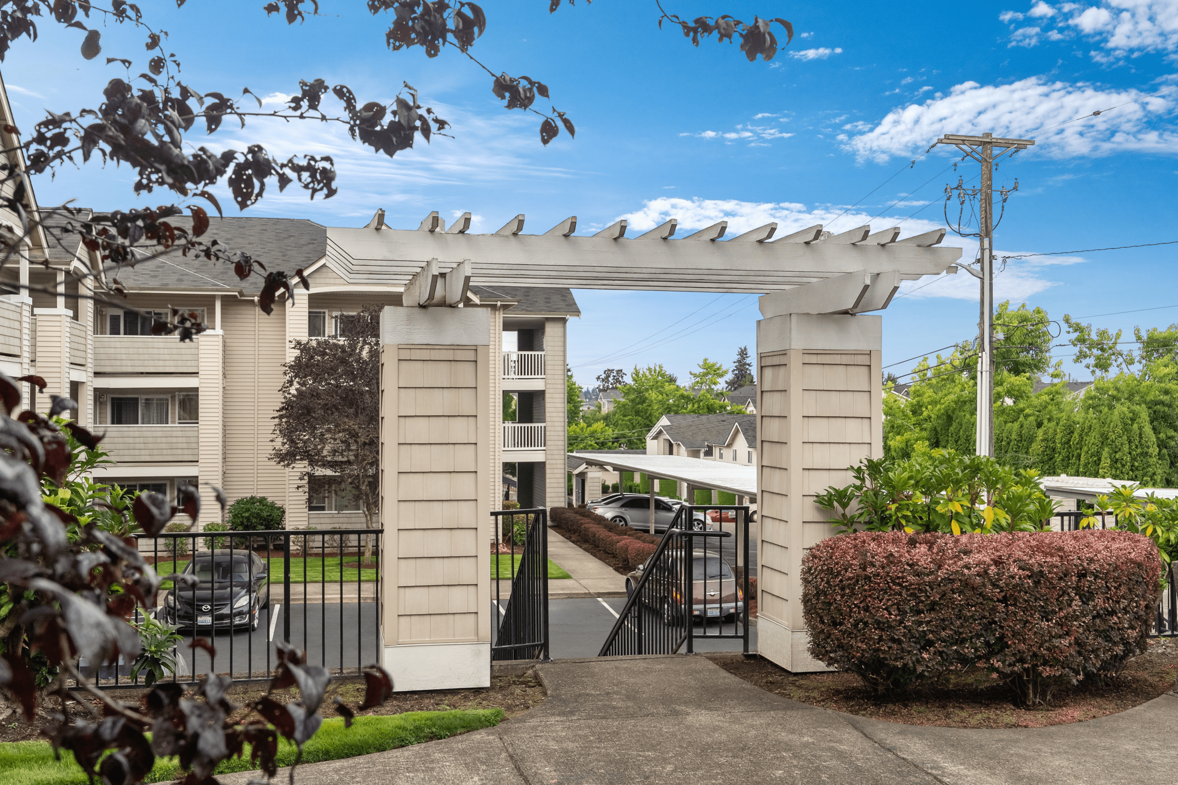 Charming apartment entrance with elegant pergola and lush landscaping under a vibrant blue sky.