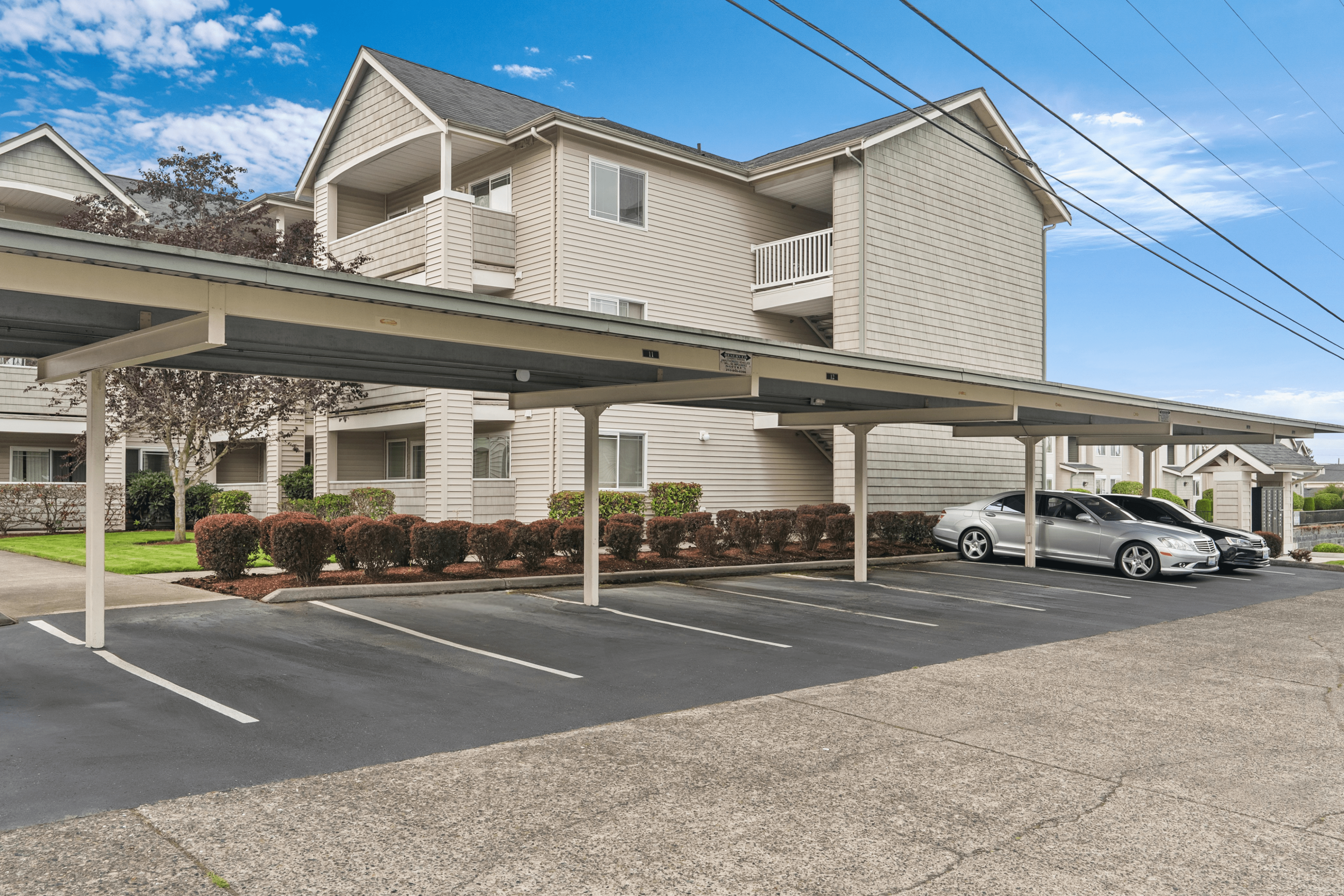 Modern apartment complex with covered parking and well-maintained landscaping under a clear blue sky.