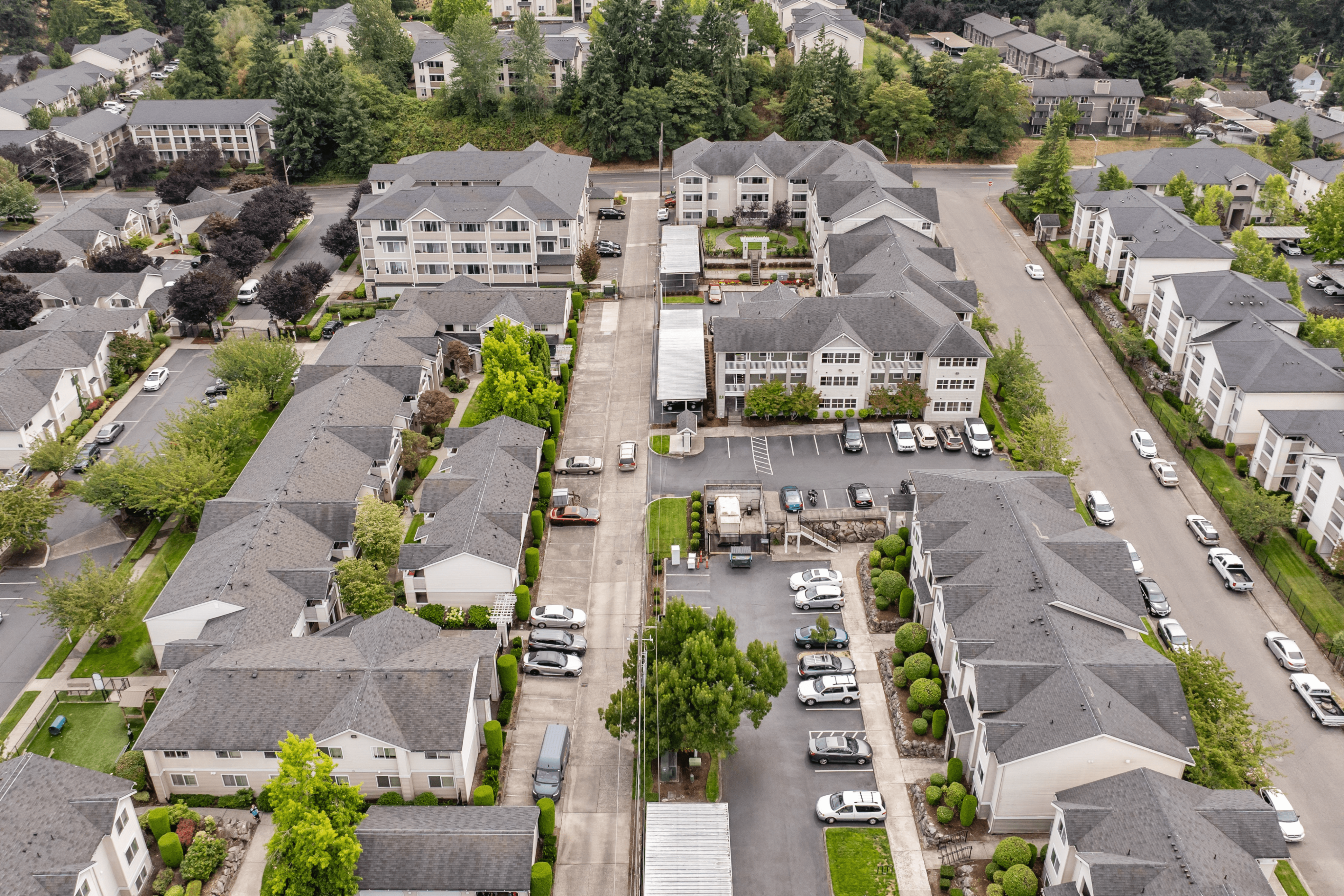 Aerial view of a charming suburban apartment complex with tree-lined streets, ample parking, and modern housing units surrounded by lush greenery.
