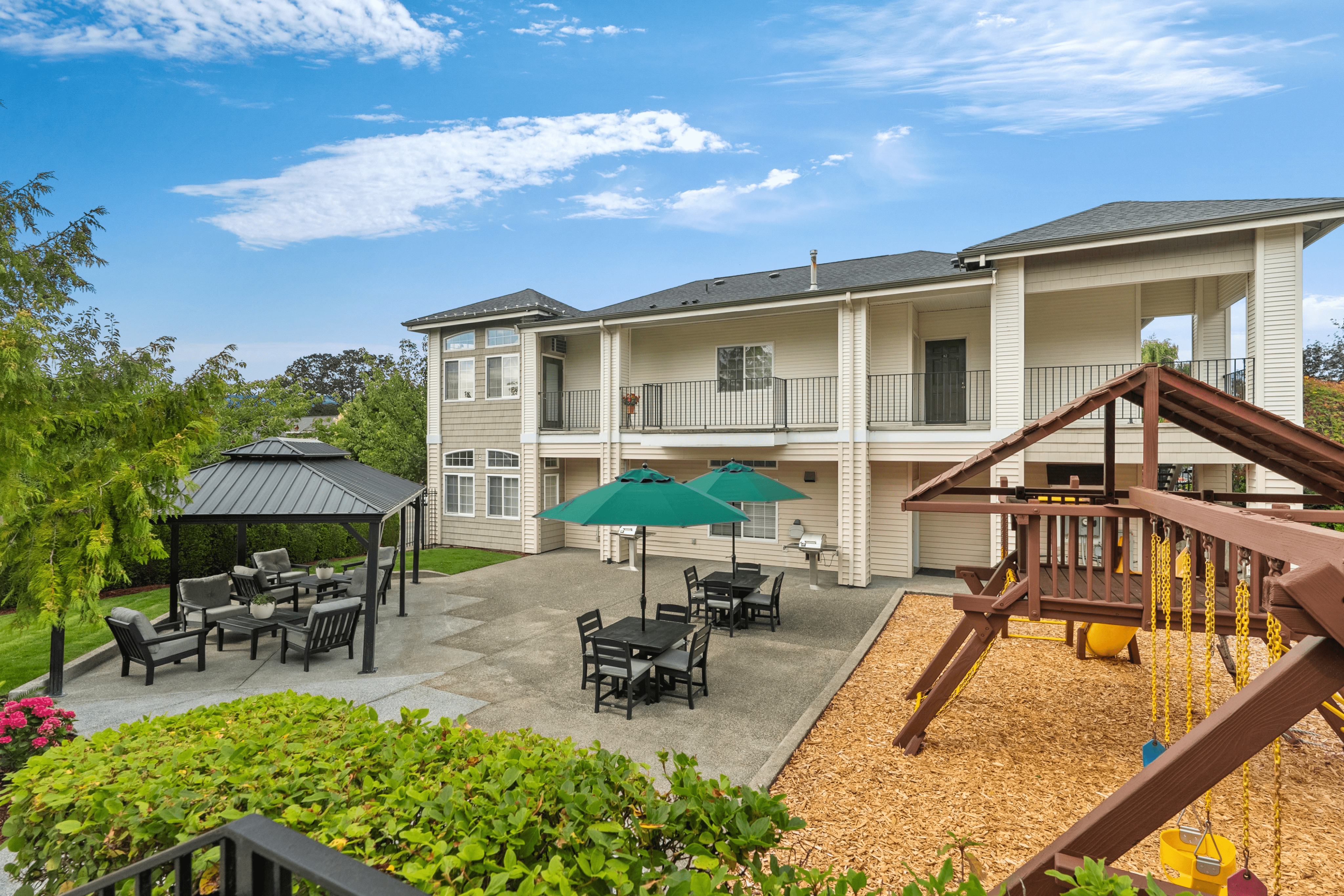 Charming apartment complex with a spacious patio area, featuring outdoor seating under stylish gazebos and umbrellas, alongside a vibrant children's playground.