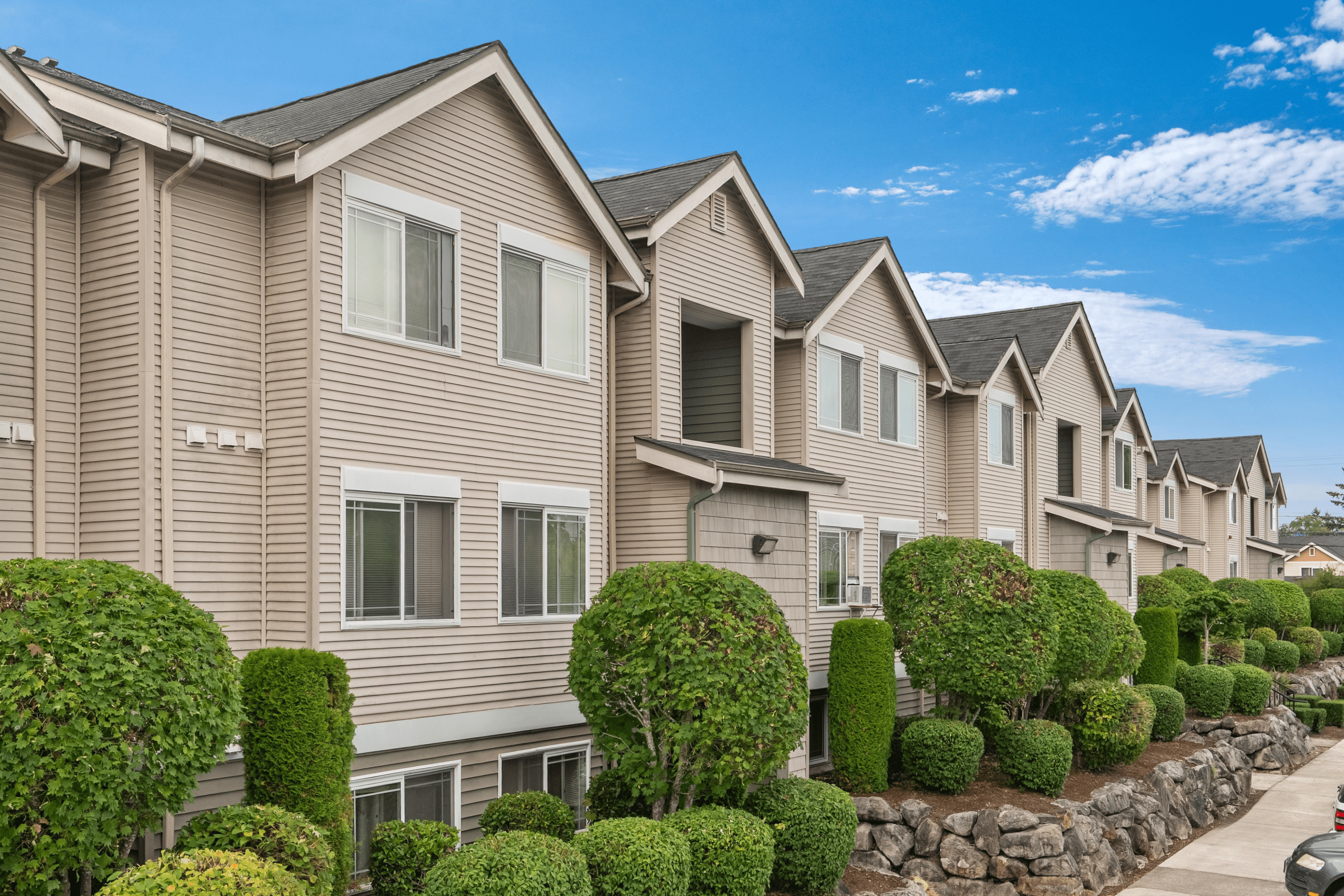 Charming townhouse complex with modern architecture, lush green landscaping, and a serene suburban setting under a bright blue sky.