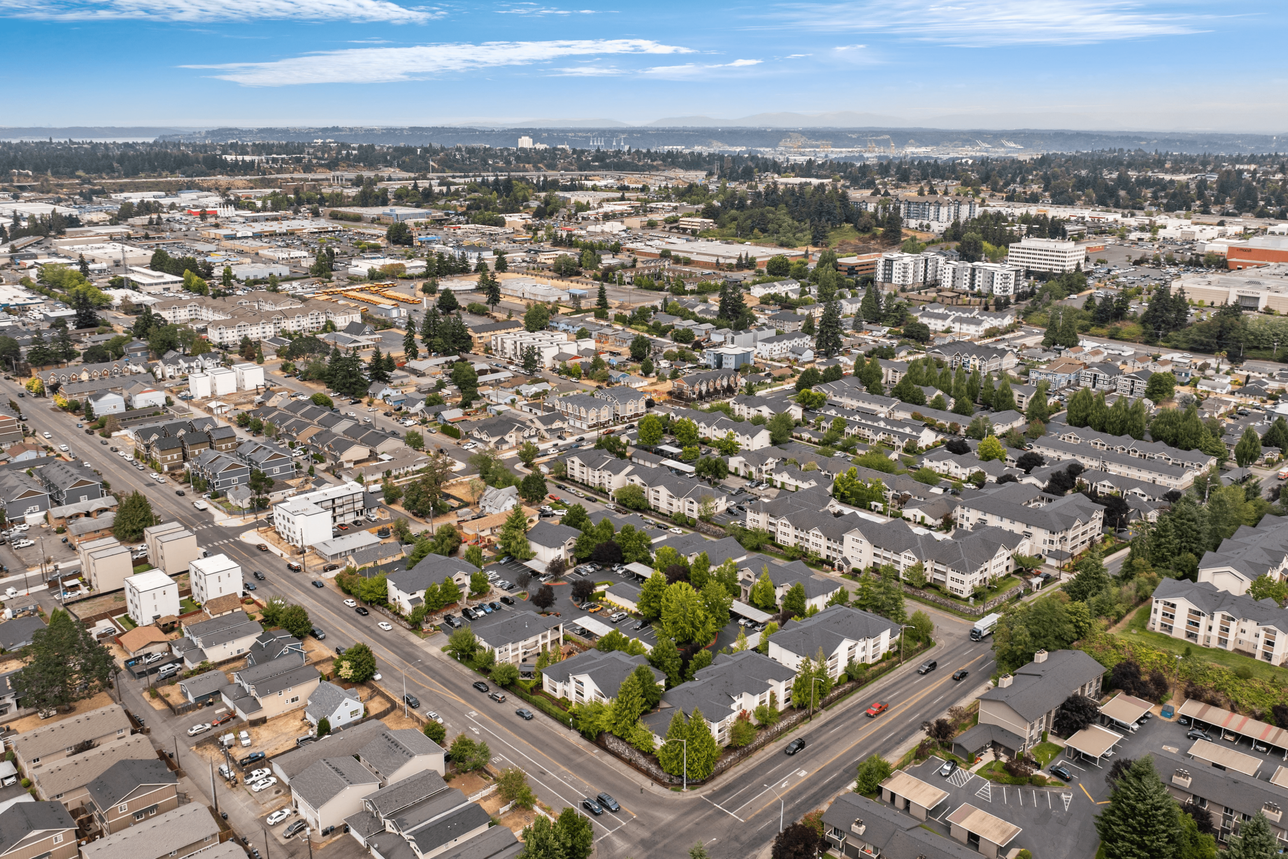 Expansive aerial view of a vibrant neighborhood showcasing lush greenery, modern apartments, and bustling streets under a clear blue sky.
