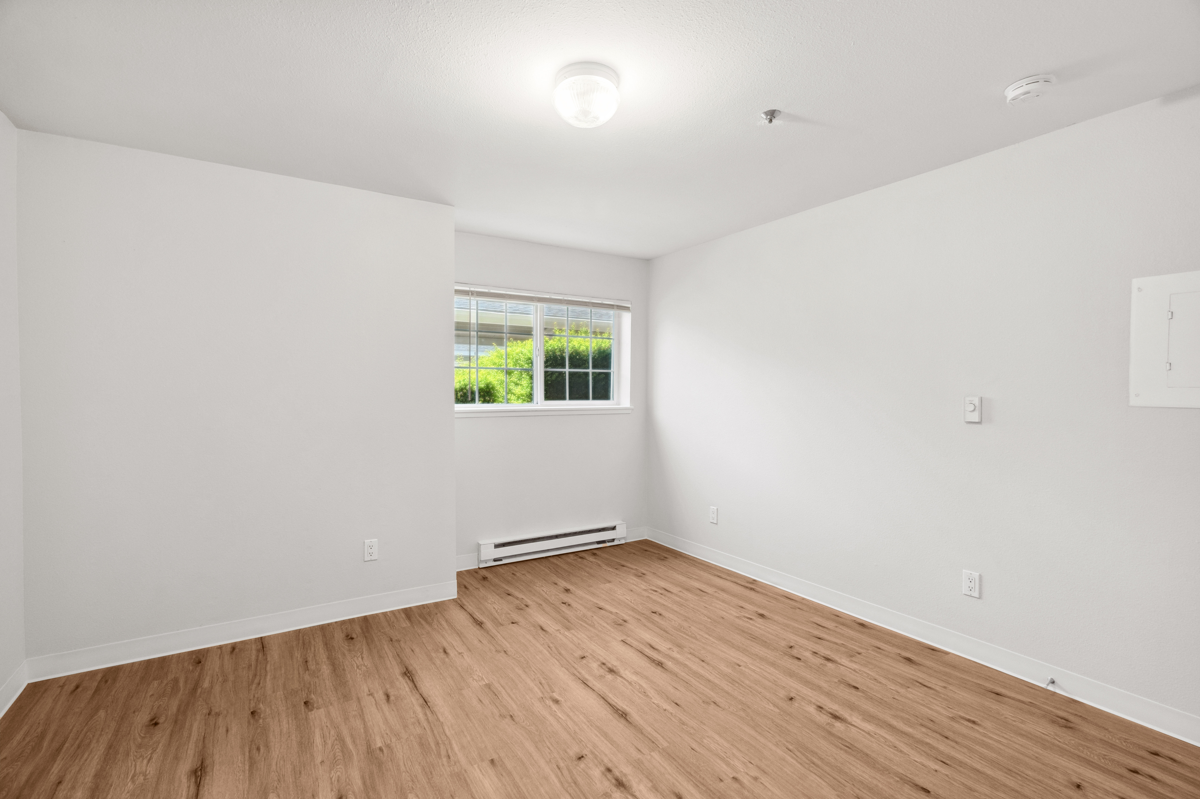 Bright and inviting empty room featuring elegant wood flooring, a modern light fixture, and a large window with abundant natural light.