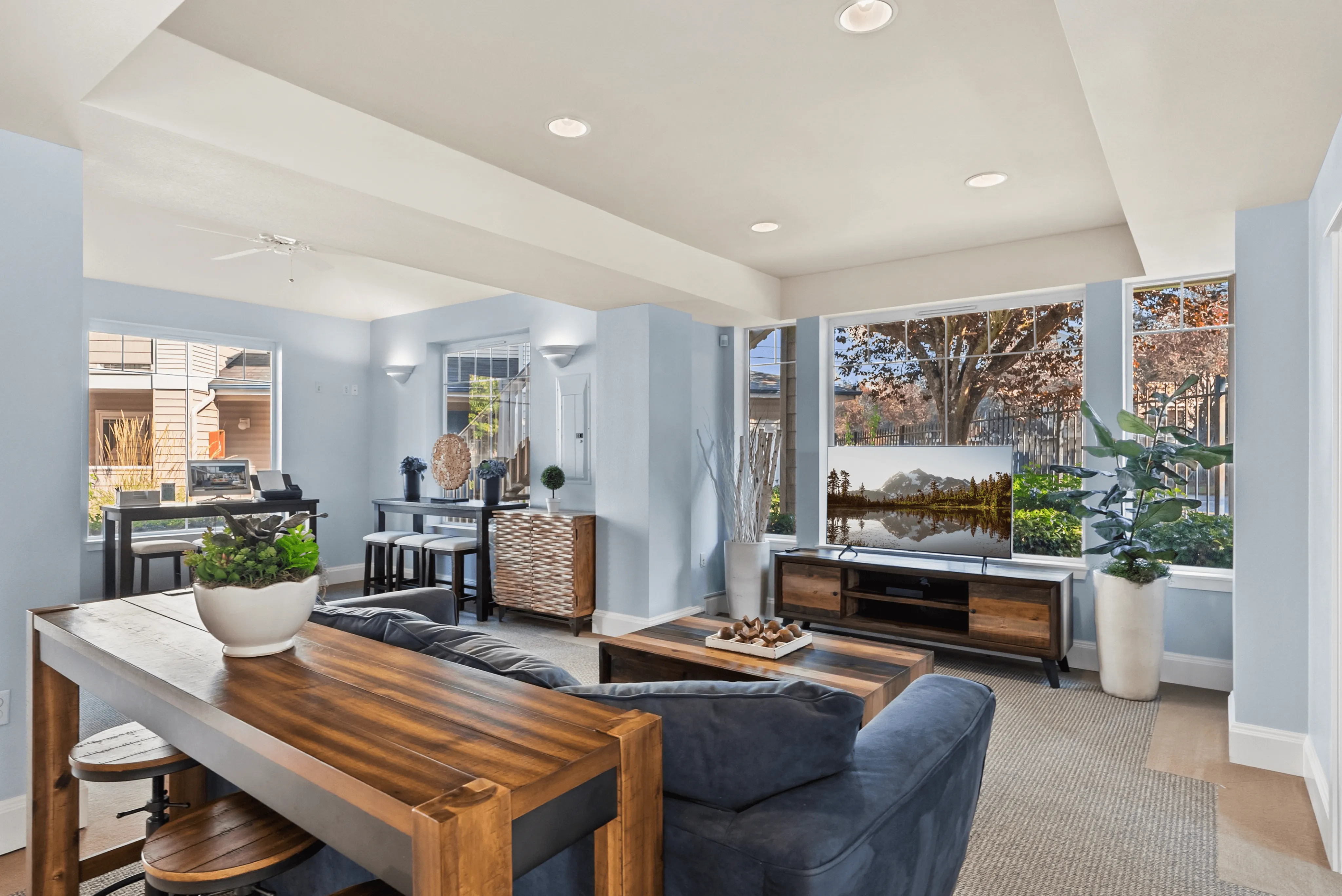 Bright and inviting living space featuring modern decor, wooden furniture, and large windows with natural light.