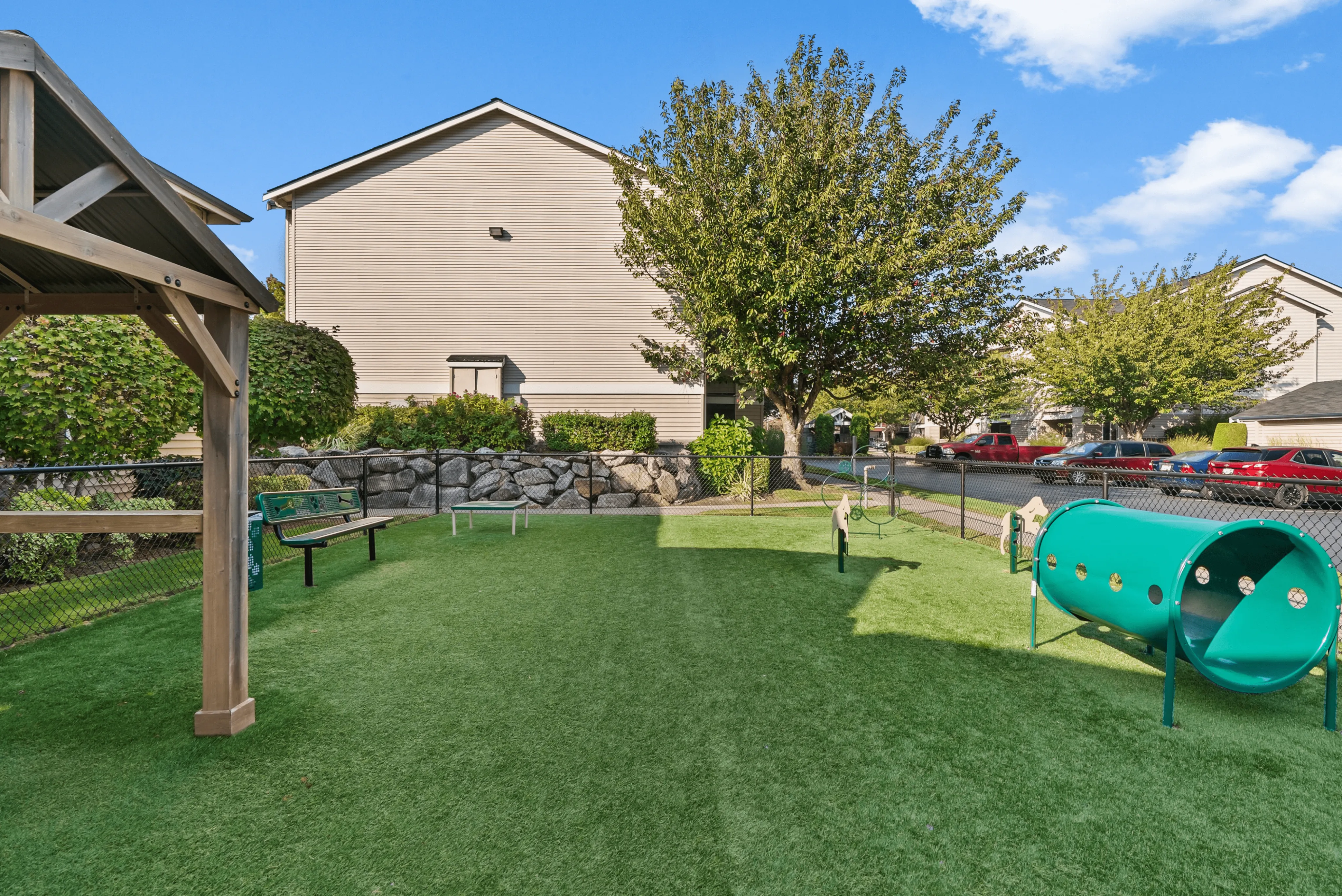 Charming outdoor play area with lush green turf, vibrant play equipment, and cozy seating under a pergola beside a residential building.