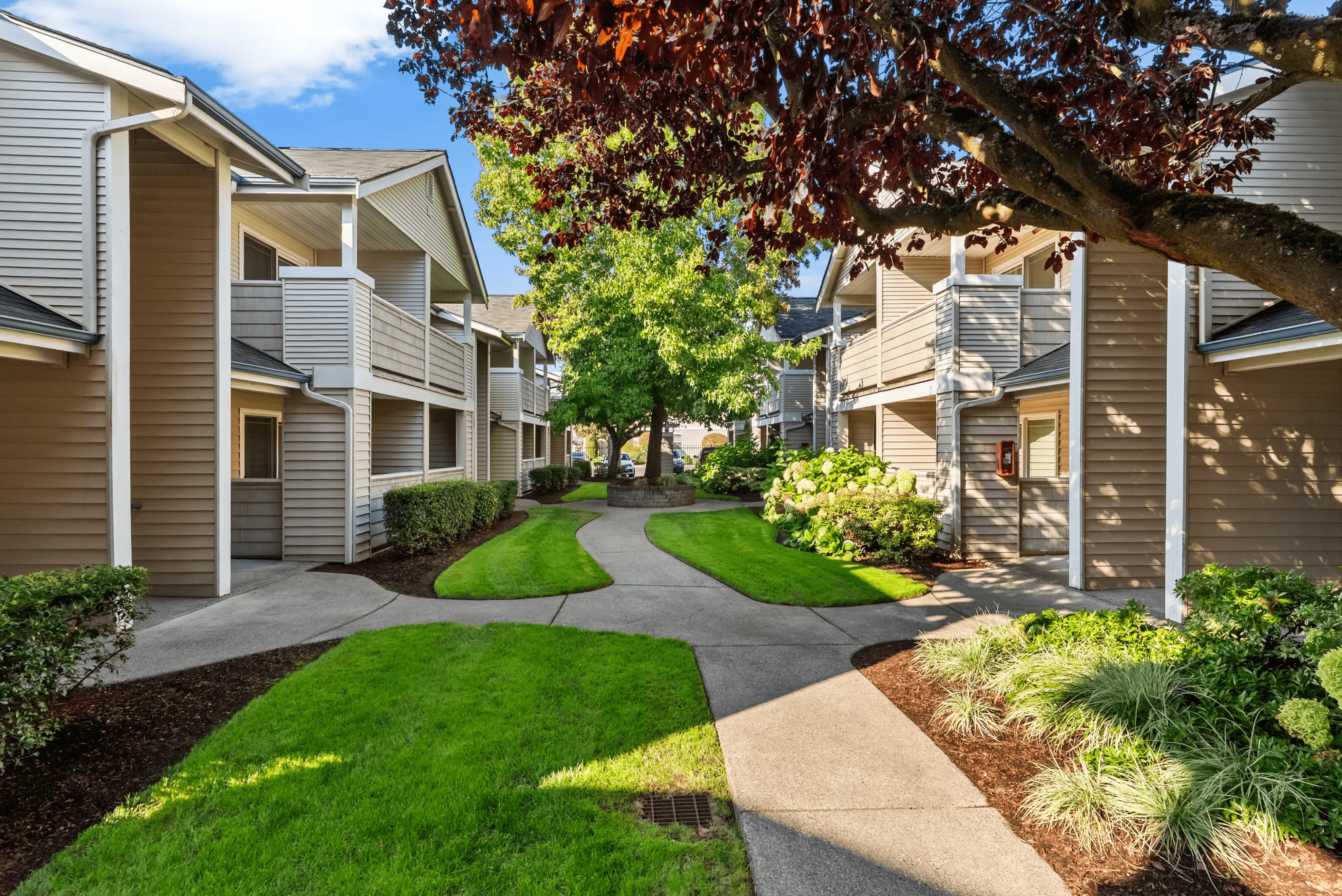 Charming apartment complex with lush landscaping and inviting pathways under a bright blue sky.