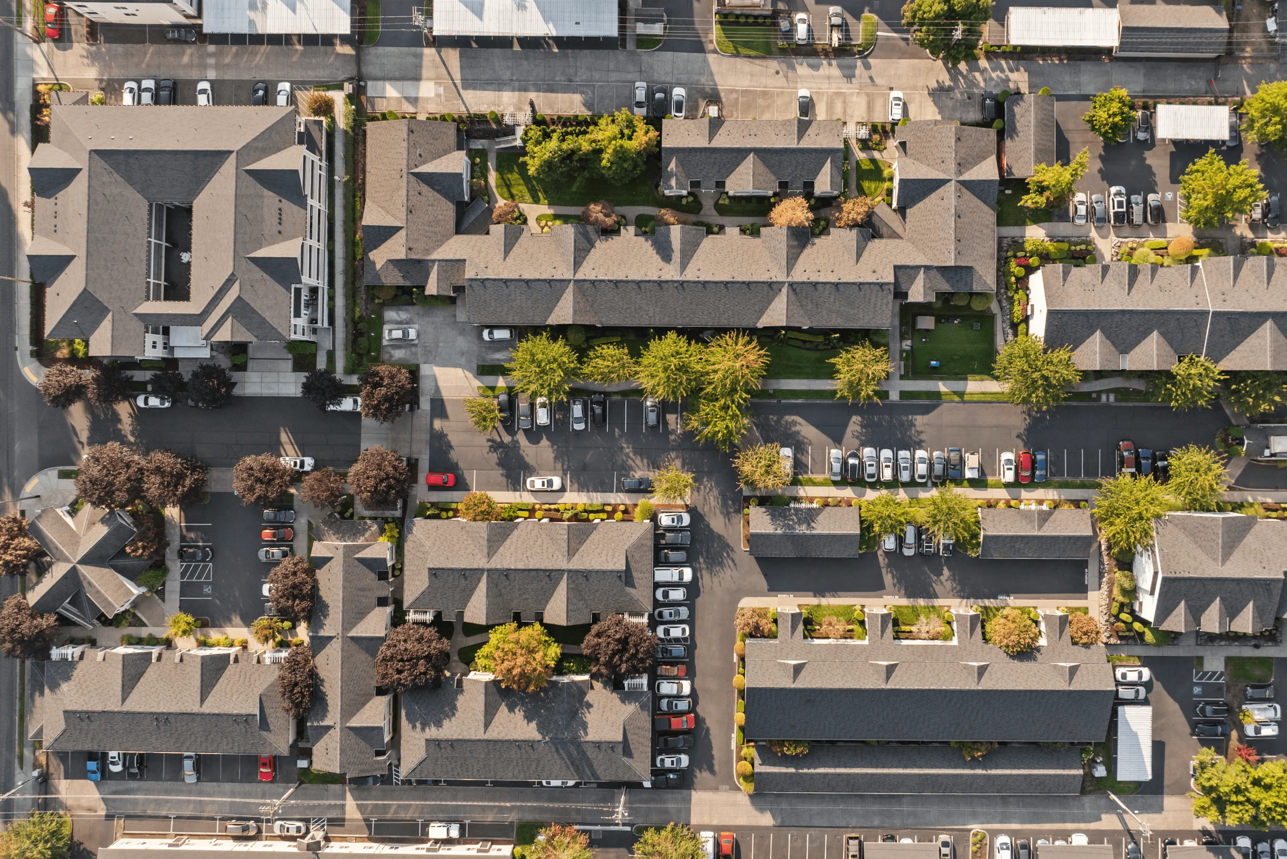 Vibrant aerial view of a modern apartment complex with lush greenery, ample parking, and stylish architecture.