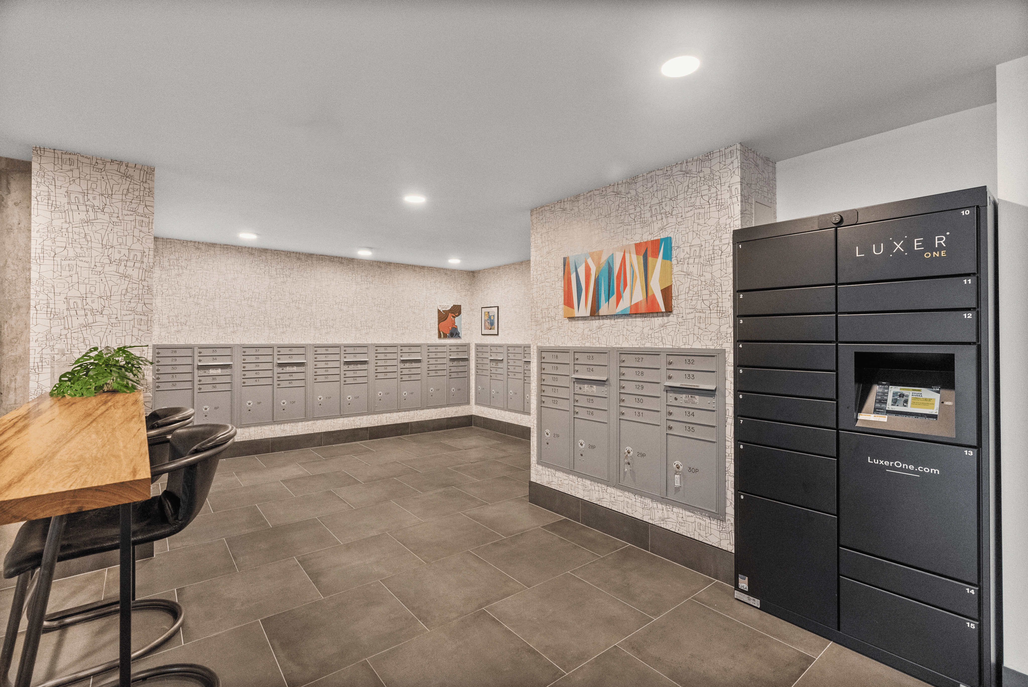 Modern mailroom with secure Luxer One locker system, chic seating, and stylish artwork, offering convenience and sophistication.
