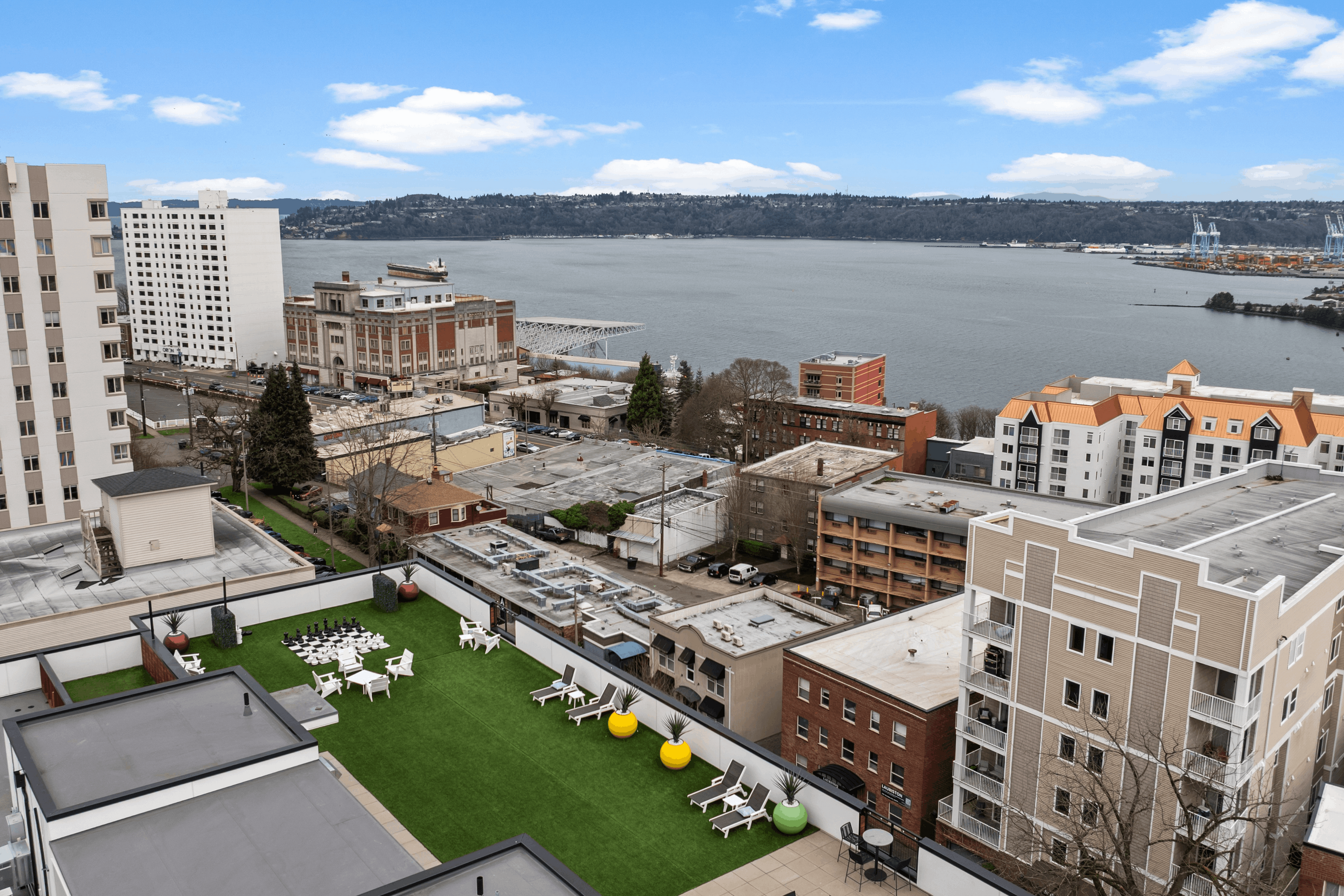 Scenic apartment view showcasing a vibrant rooftop garden with lounge chairs overlooking a stunning waterfront and city skyline.